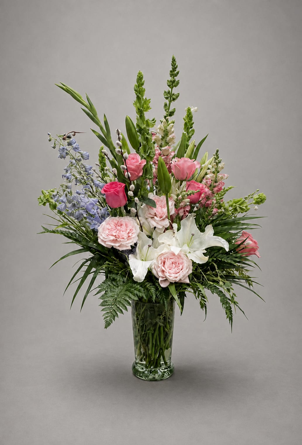 Tall mixed bouquet in a clear glass vase with pink, white, and blue flowers