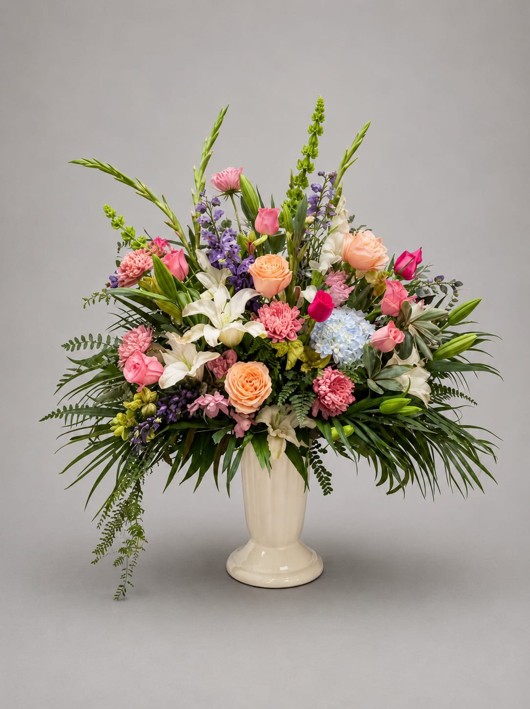 Large mixed flower arrangement in a white pedestal vase