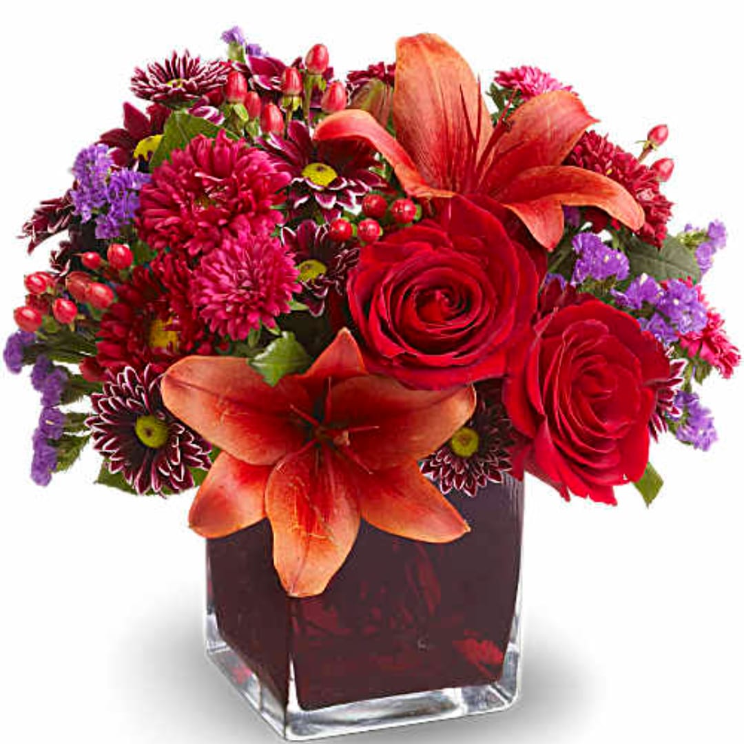 Red and orange mixed flower arrangement in a square glass vase