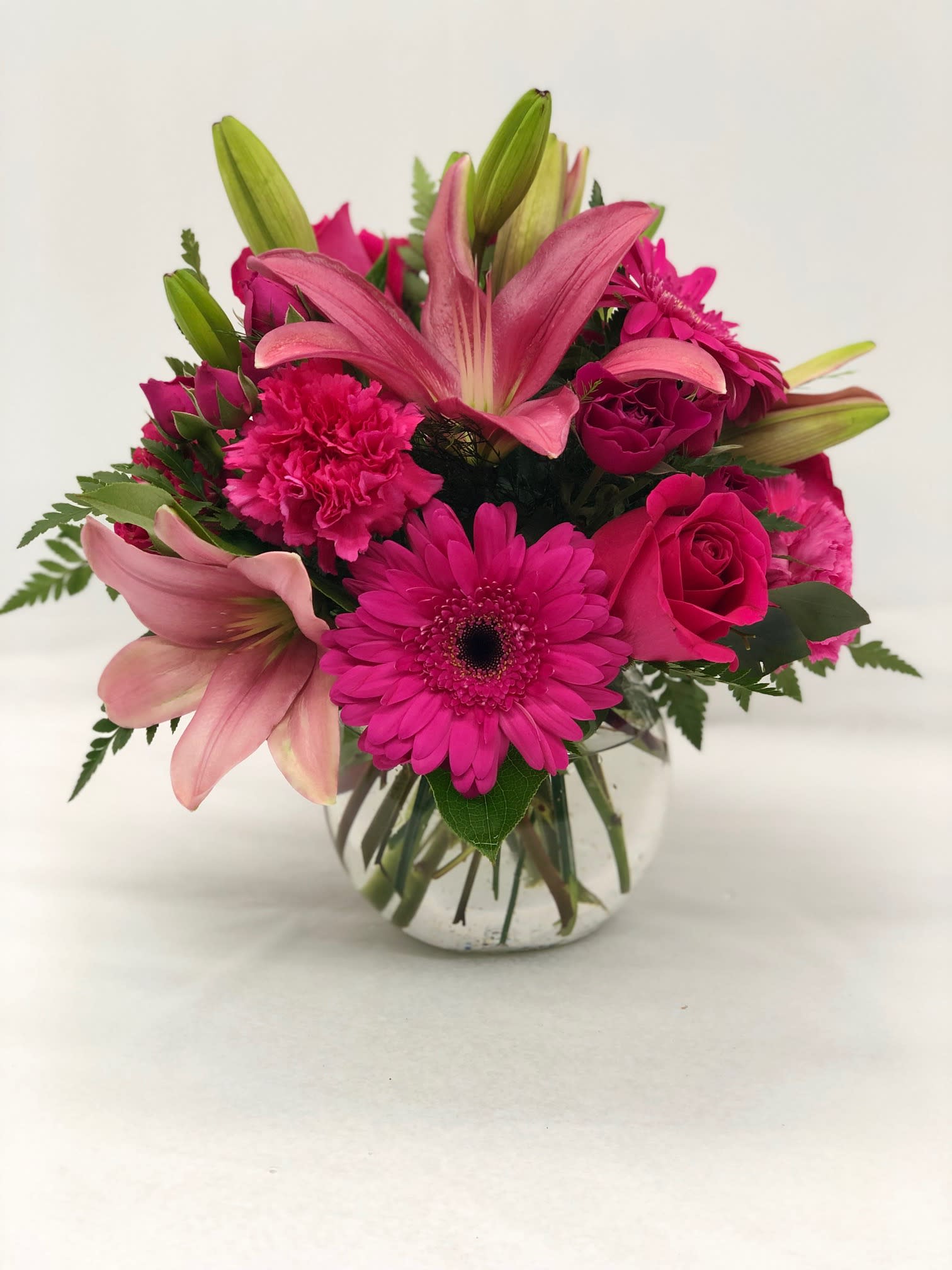 Bright pink lilies, gerbera daisies, roses, and carnations in a clear round glass vase