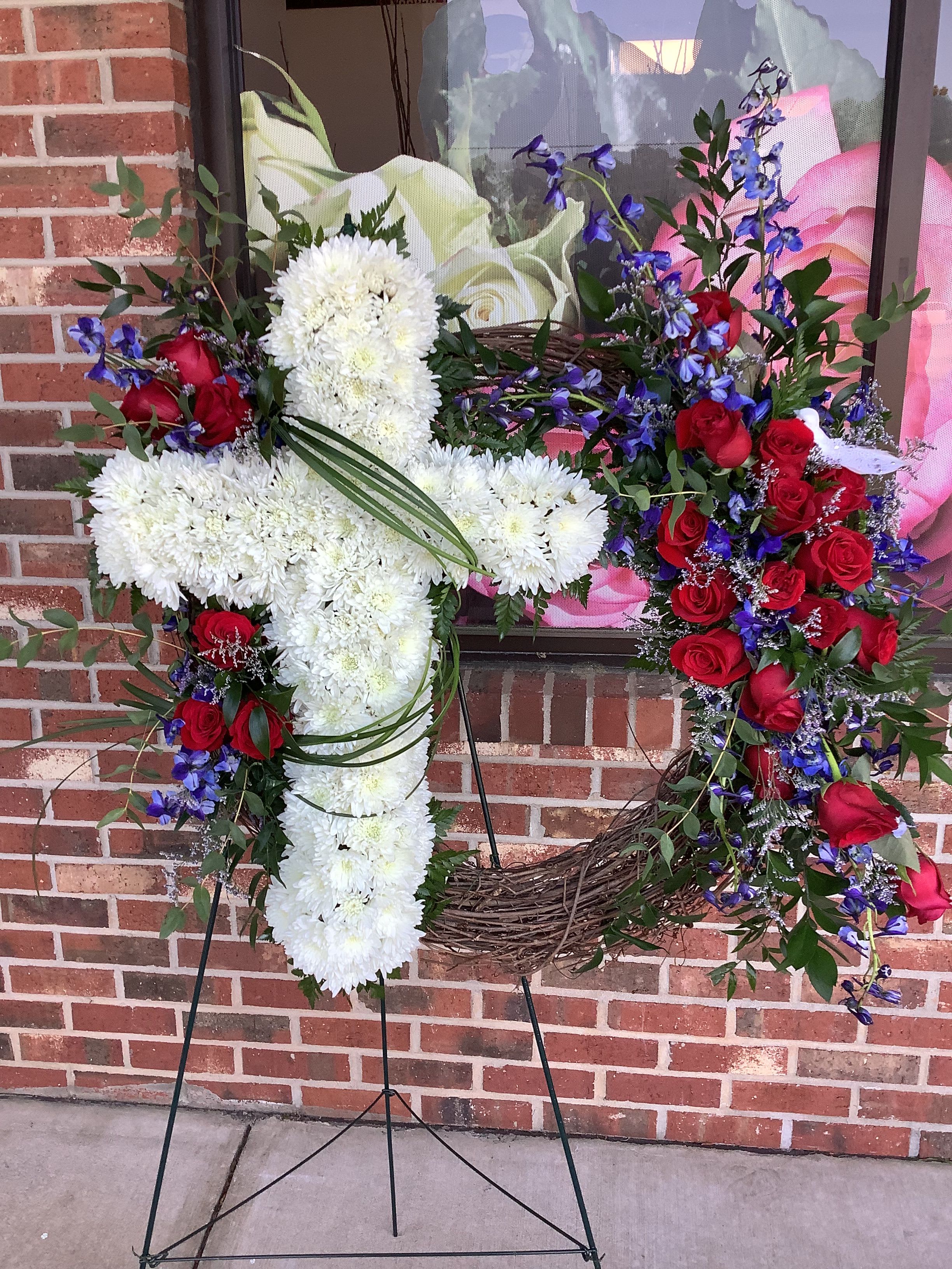 Two floral wreaths on stands, one white cross and one red rose heart