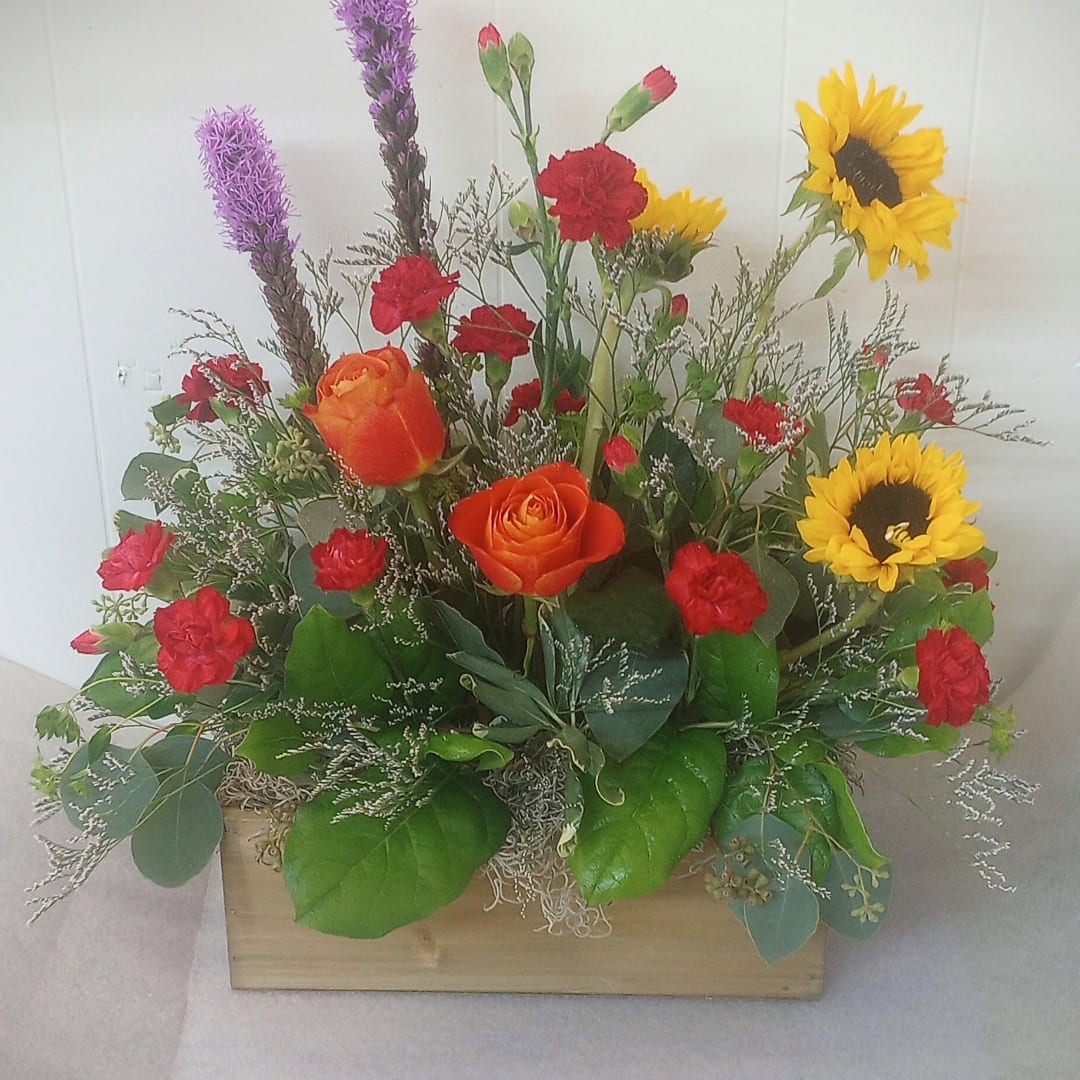 Mixed bouquet with orange roses, red carnations, and yellow sunflowers in a wooden box