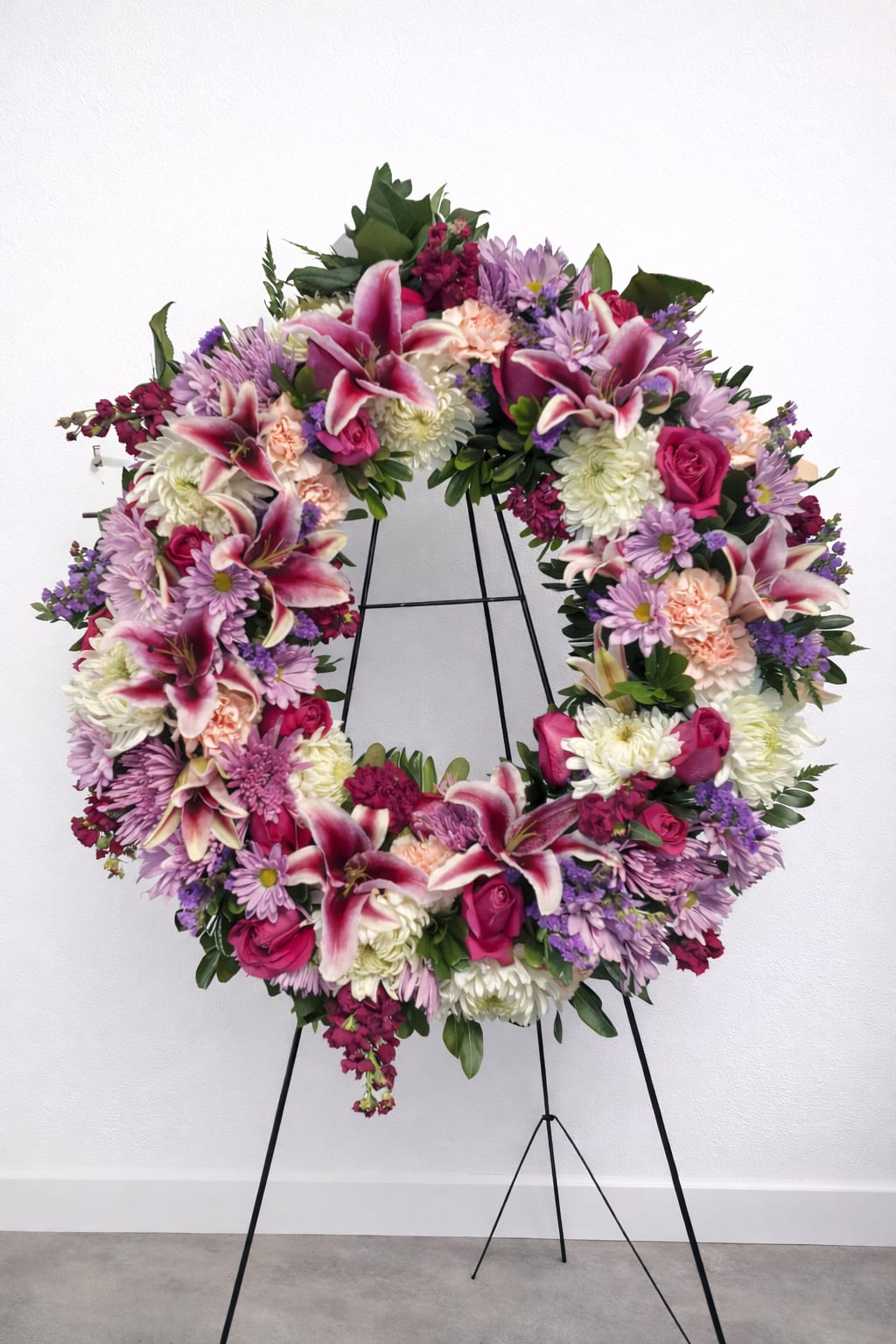 Large floral wreath with pink lilies, roses, and purple daisies on a stand