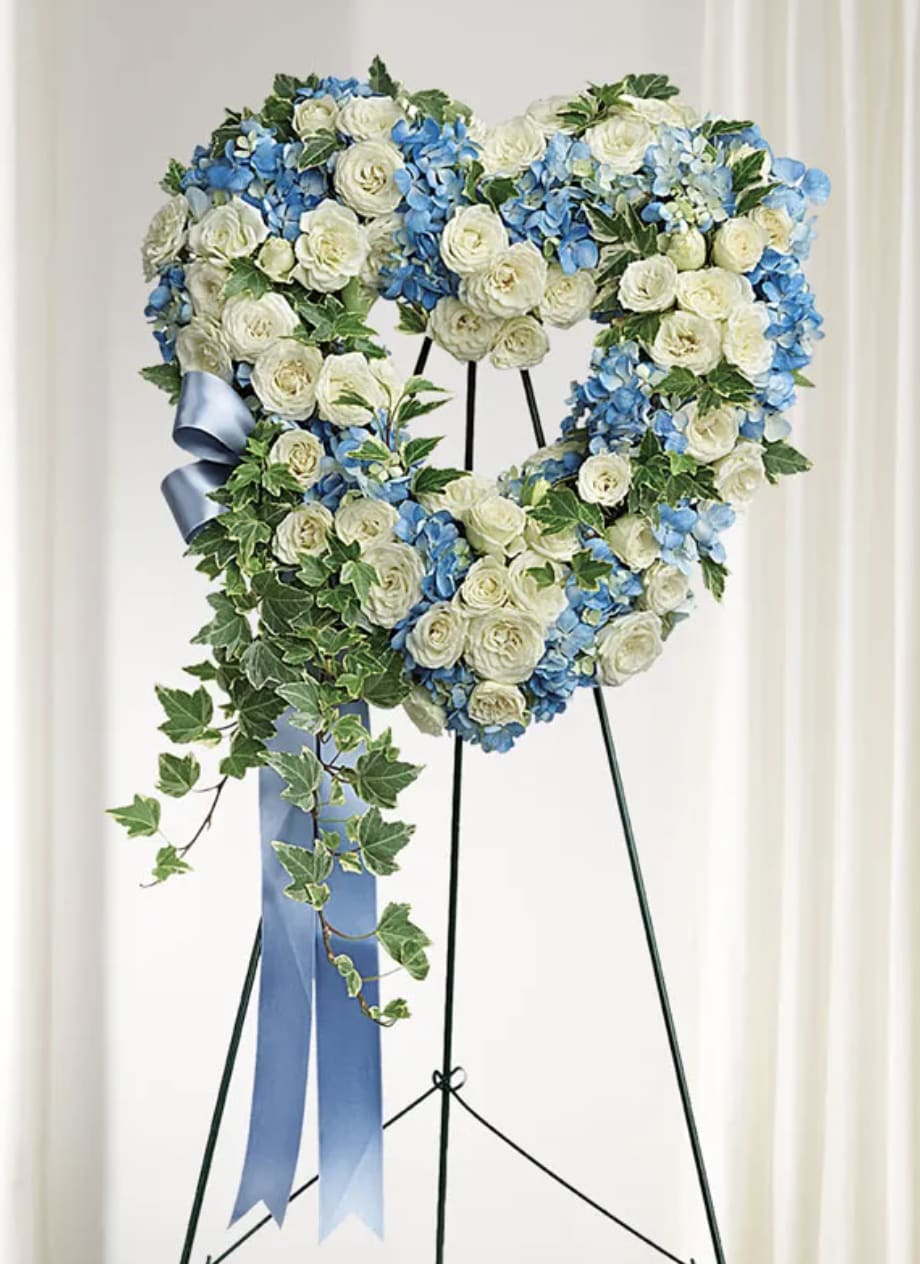 Heart-shaped floral wreath of white and blue flowers on a stand