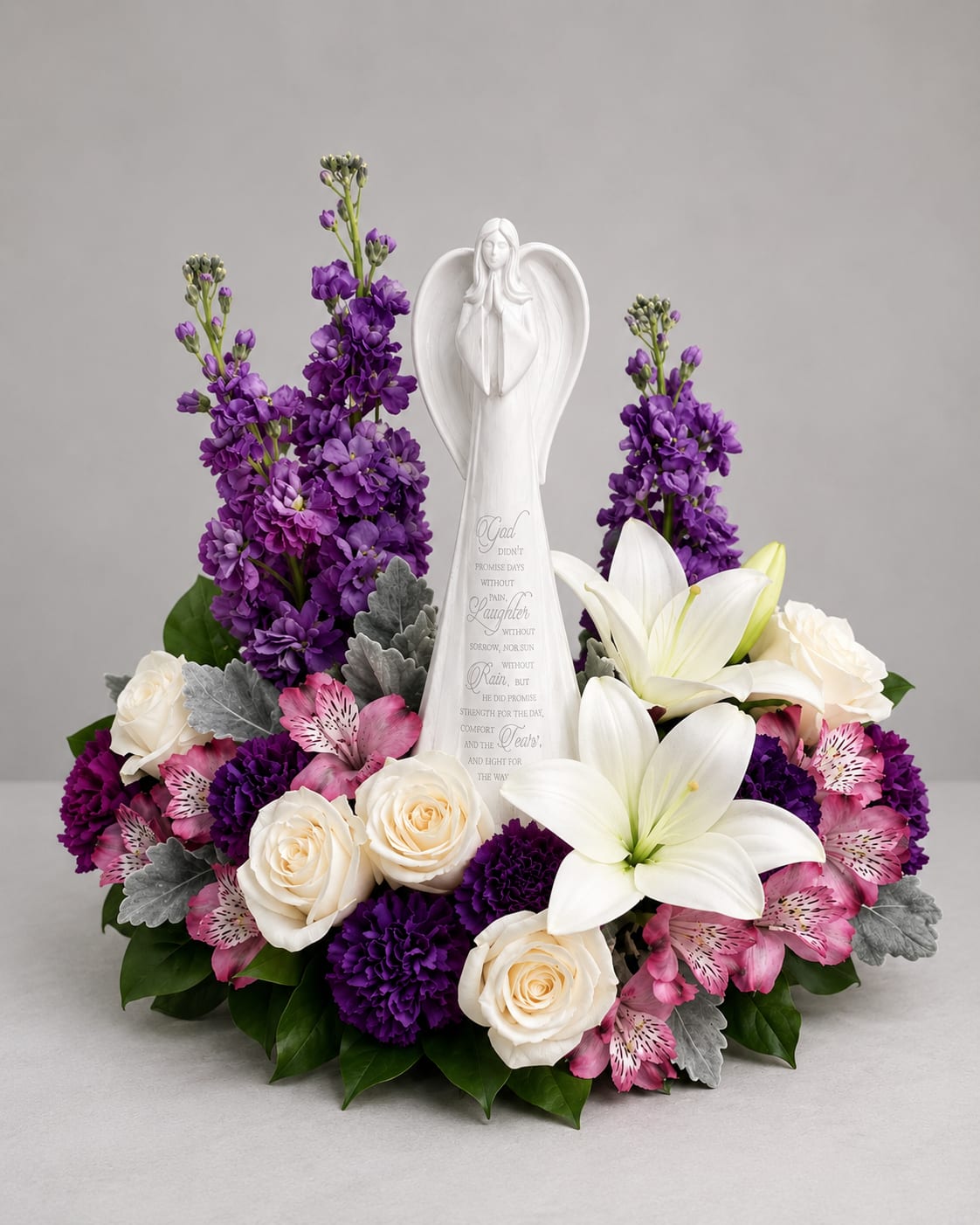Beautiful Heart Angel  - how them they're in your heart with this magnificent display of roses, lilies and alstroemeria, gracefully surrounding a timeless angel sculpture keepsake. Beautifully fragrant, it's a tribute that will warm their hearts forever. This beautiful arrangement includes crème roses, white asiatic lilies, lavender alstroemeria, purple carnations, lavender stock, dusty miller and lemon leaf. 