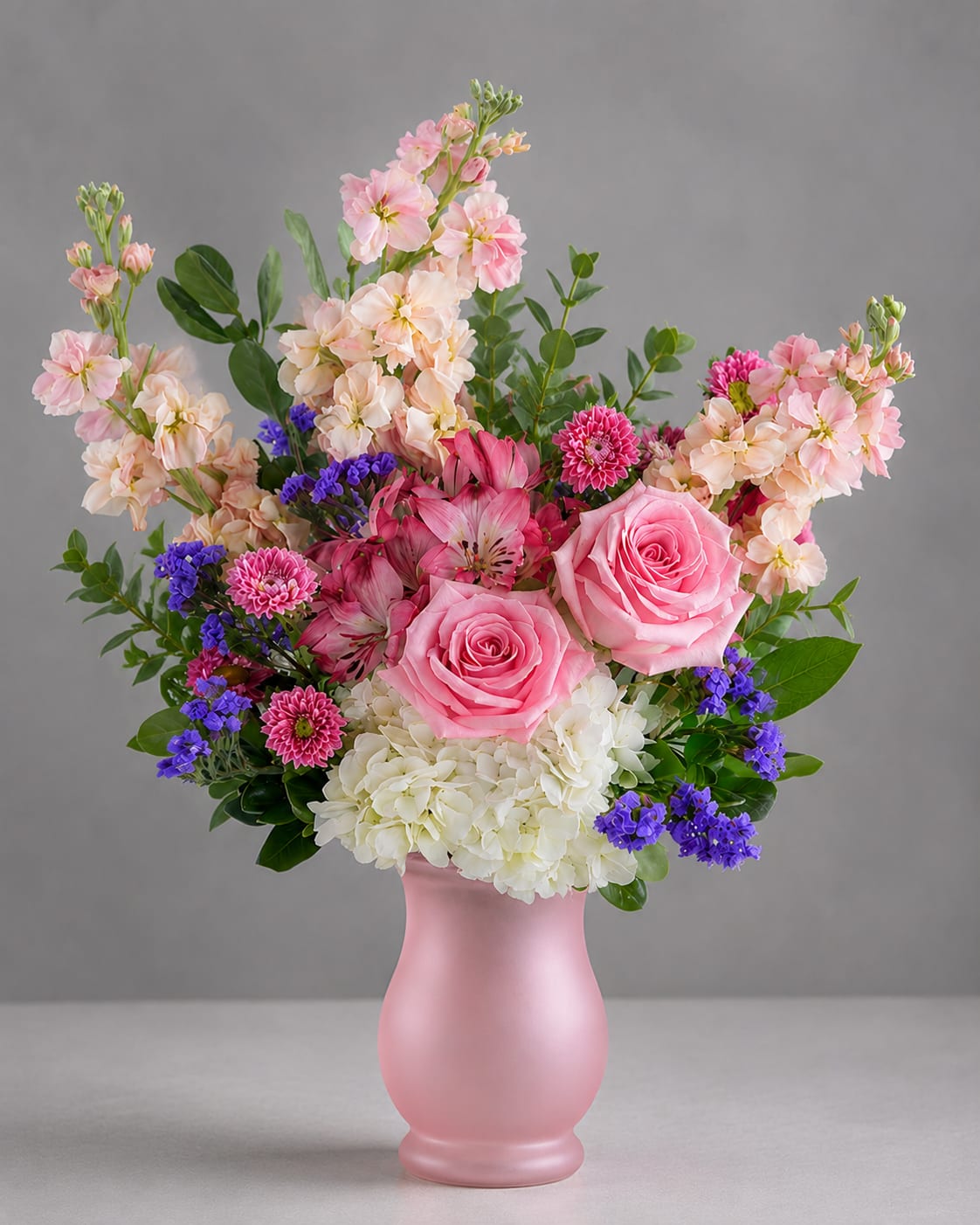 Pink Harmony  - Flowers are arranged loose and abundant in a clear glass vase so stems and water show through for a natural, airy look; greenery branches outward to give the design a relaxed, garden feel. The combination balances long-lasting, sturdy blooms (chrysanthemums and carnations) with fragrant, romantic stock and delicate asters-an everyday bouquet that still feels special for Women's Day, Best Friends Day, or Admin Professionals' Week. Simple care-fresh water and a clean vase-keeps the mix looking its best.  4W x 7H Vase Size
