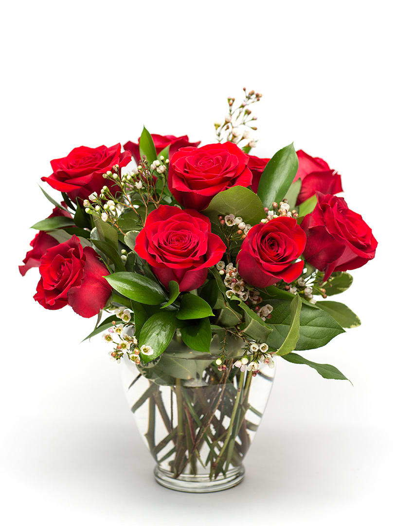 Red roses arranged in a clear glass vase with small white filler flowers