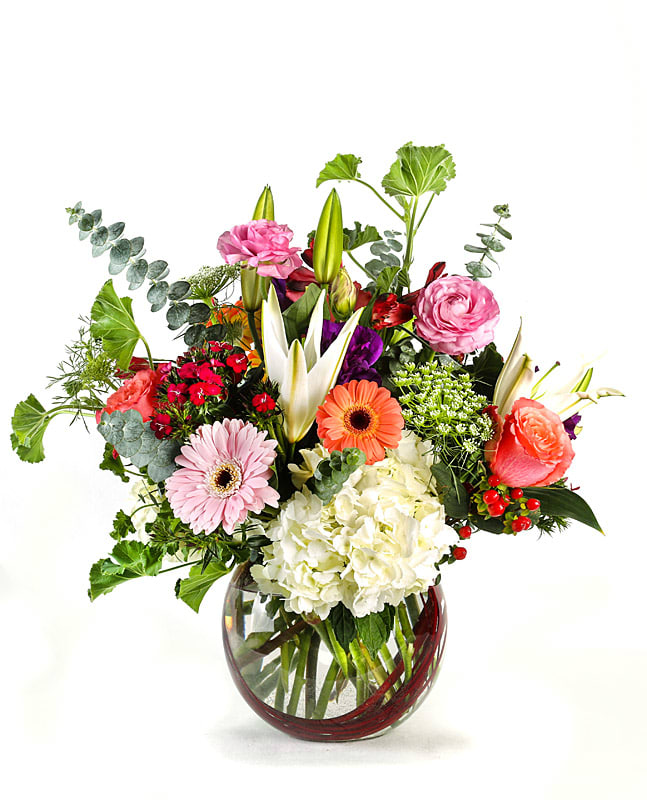 Mixed bouquet in a round glass vase with pink, white, orange, and red flowers