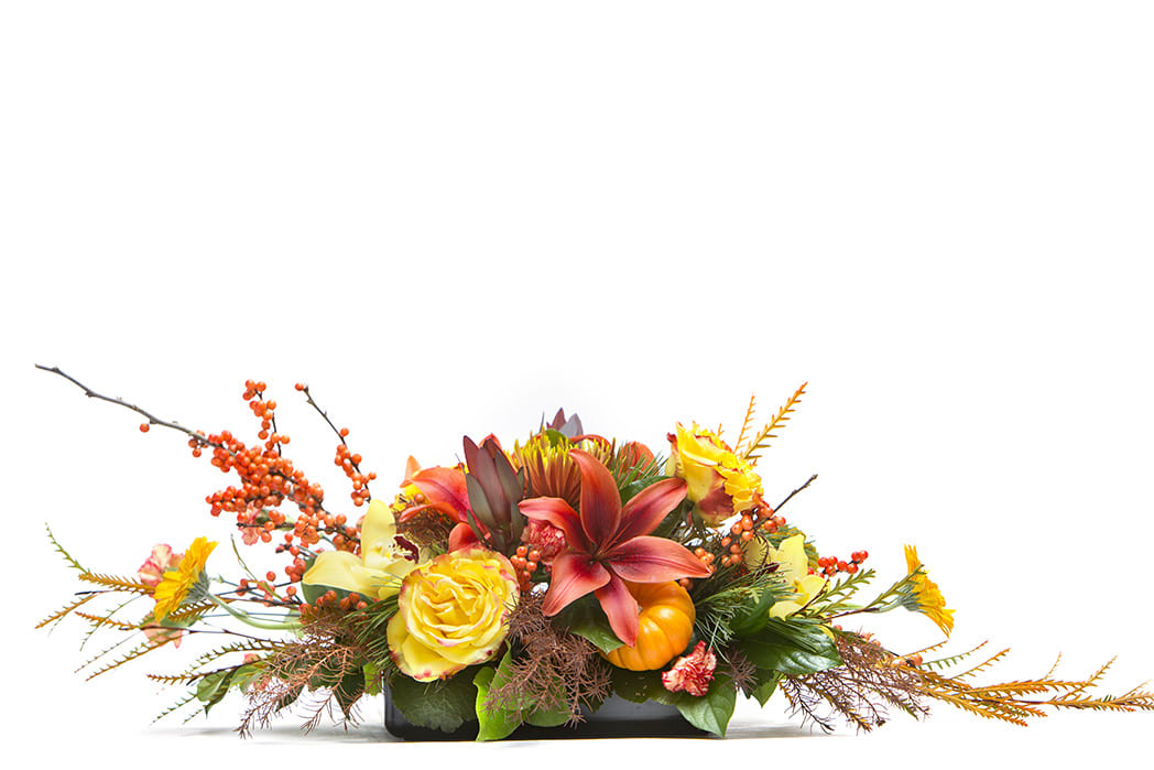 Low floral arrangement with yellow roses, orange lilies, and autumn berries in a black container