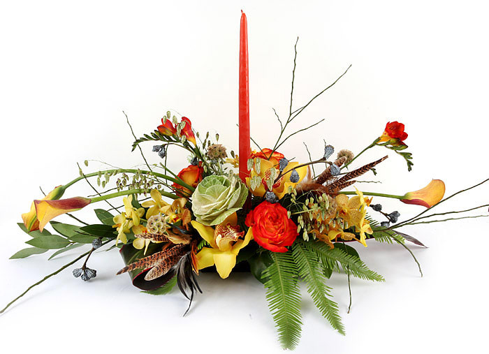 Low floral centerpiece with red candle, orange and yellow blooms, and fern accents