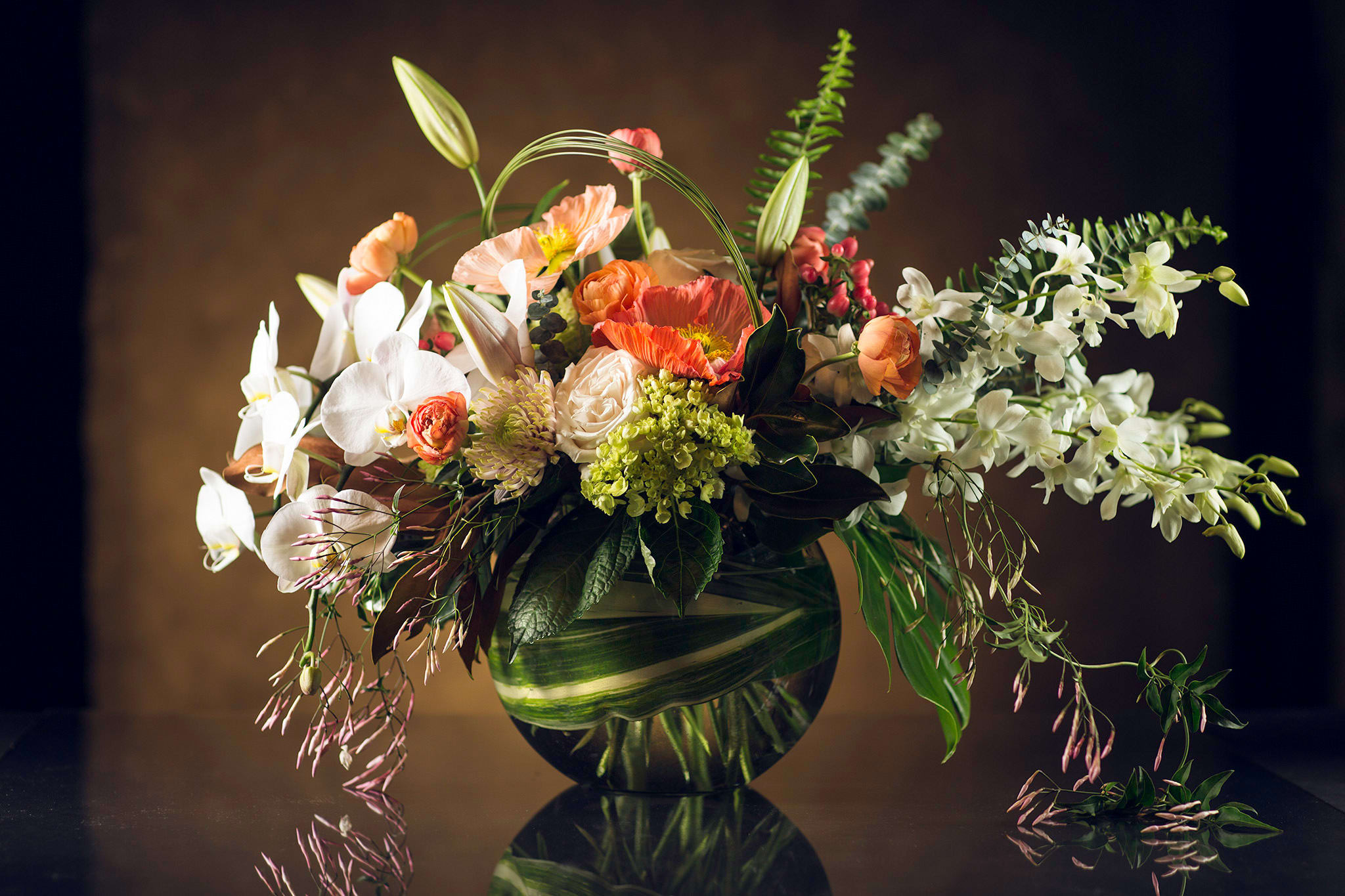 Mixed floral arrangement in a round glass vase with white orchids and orange poppies
