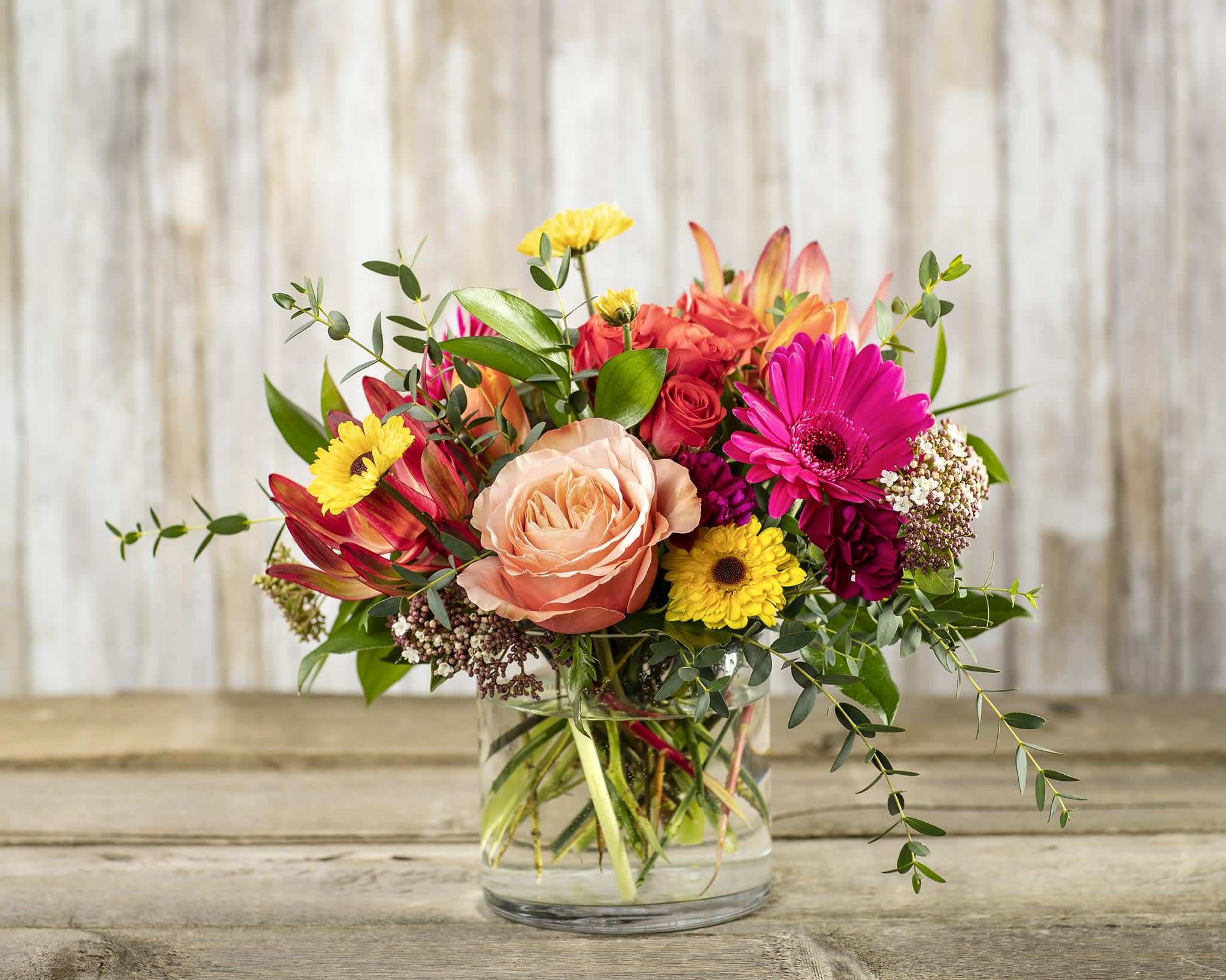 Mixed bouquet of roses, gerbera daisies, and other flowers in a glass vase