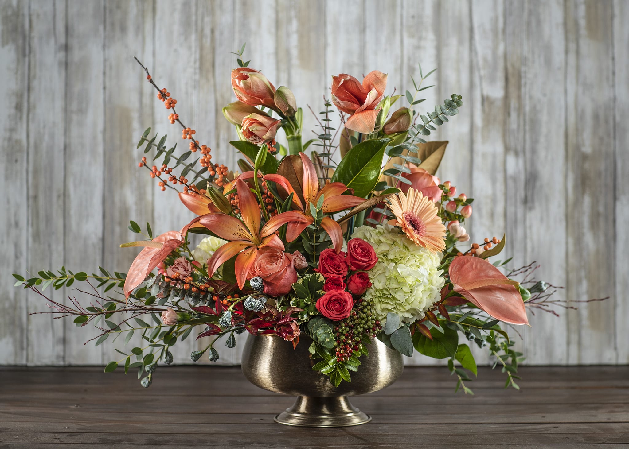 Coral lilies and red roses in a gold pedestal vase