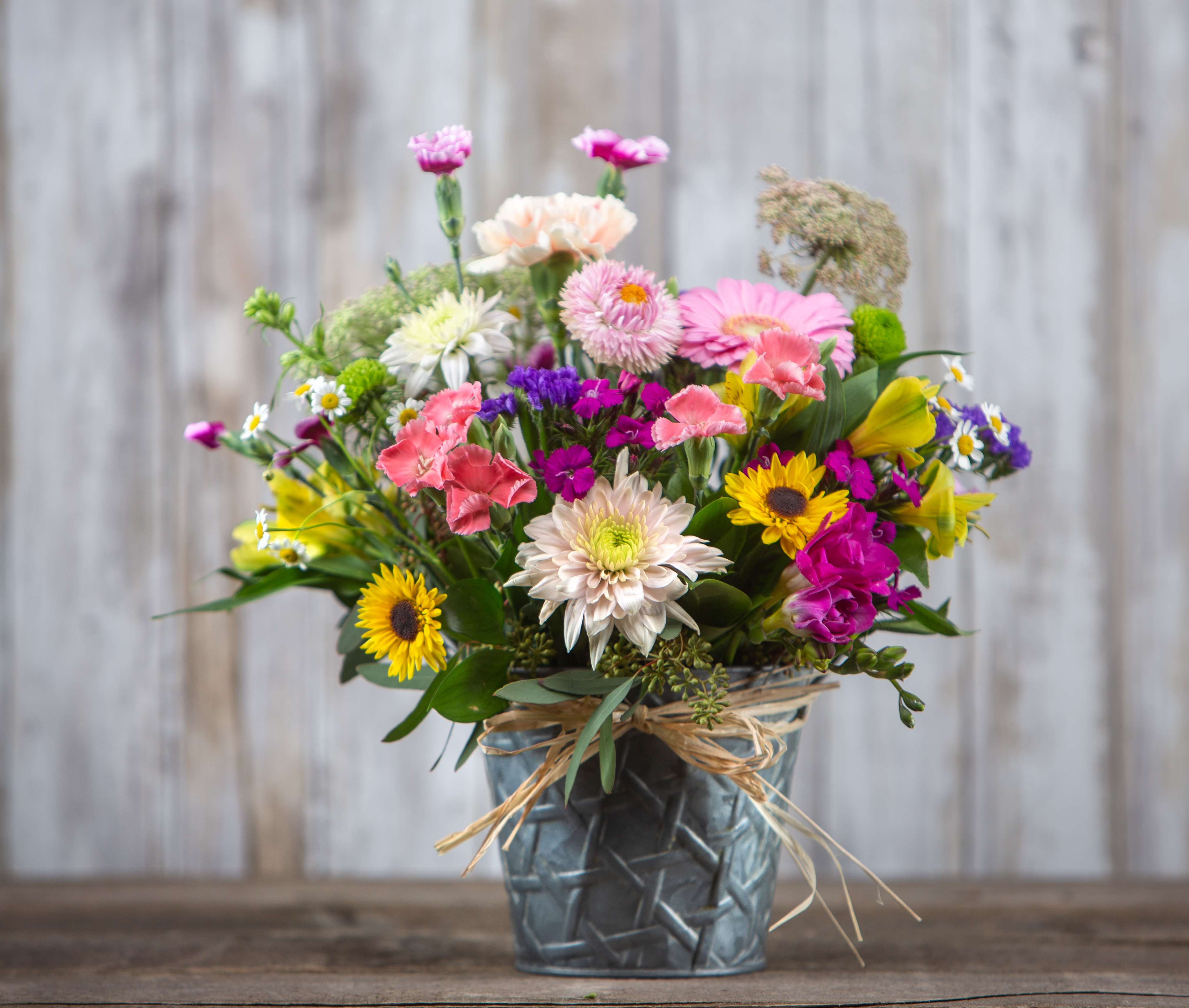 Mixed bouquet of colorful flowers in a metal vase with a raffia bow