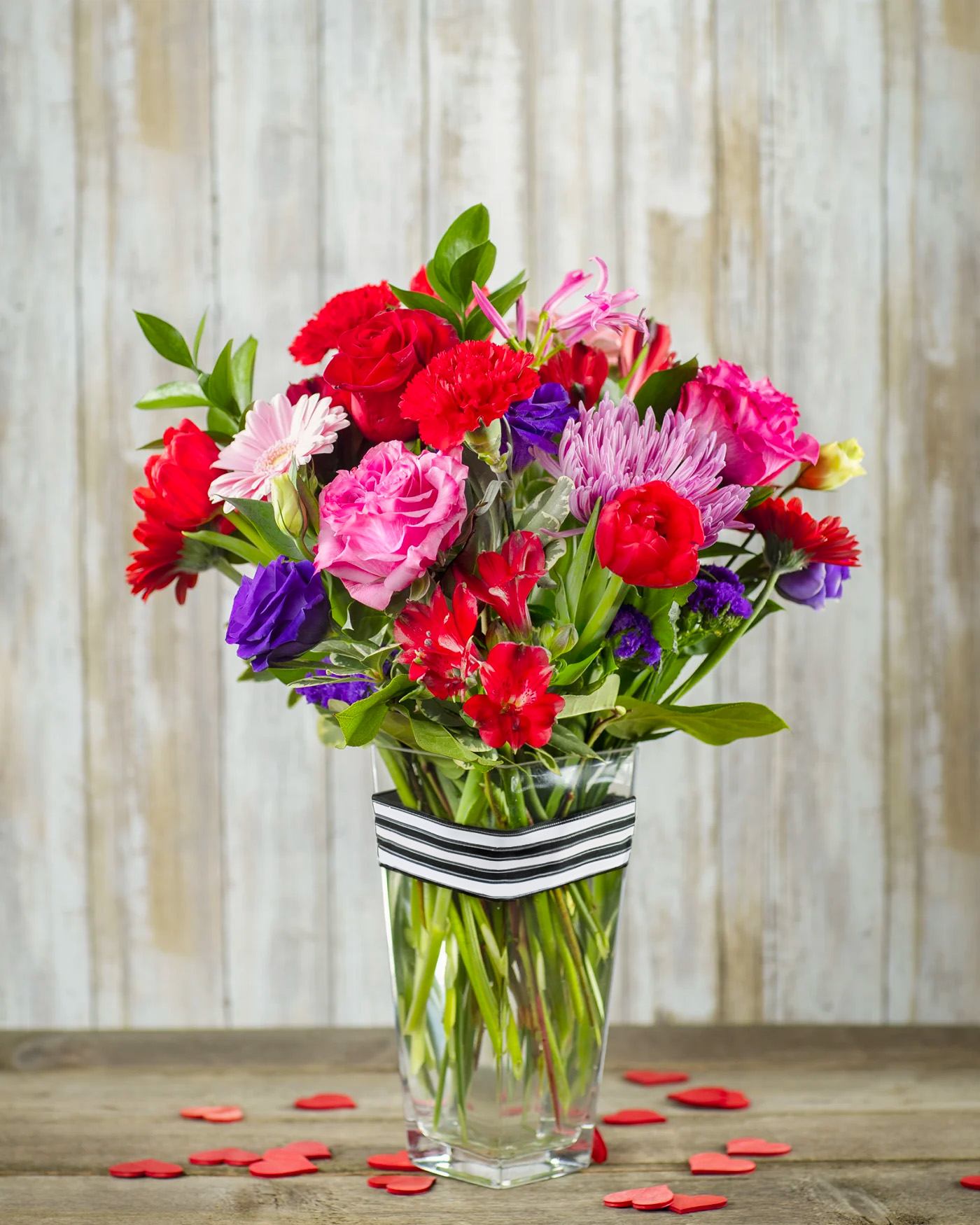 Mixed bouquet of red, pink, purple, and white flowers in a clear vase