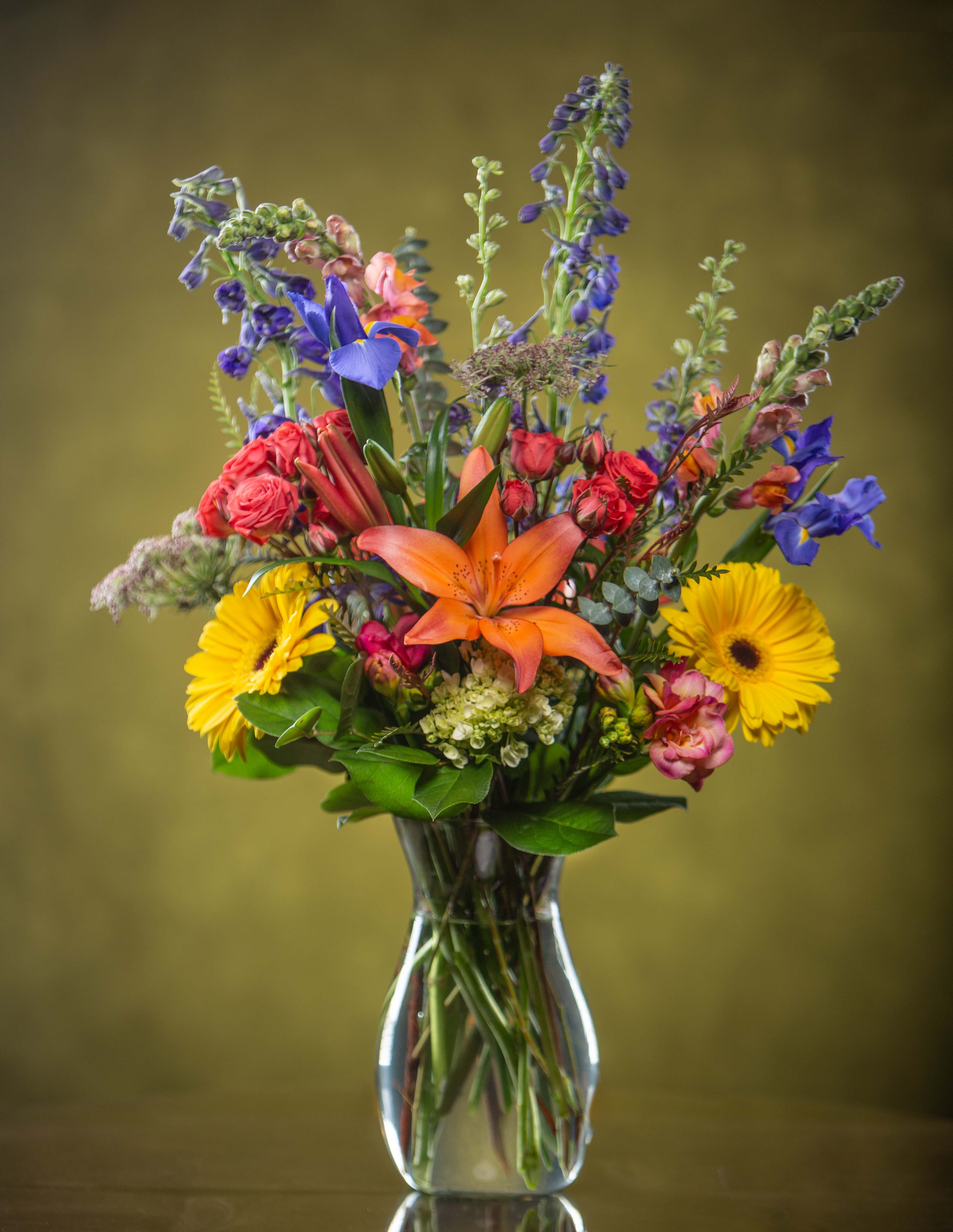 Mixed bouquet in a clear glass vase with orange lilies and yellow daisies