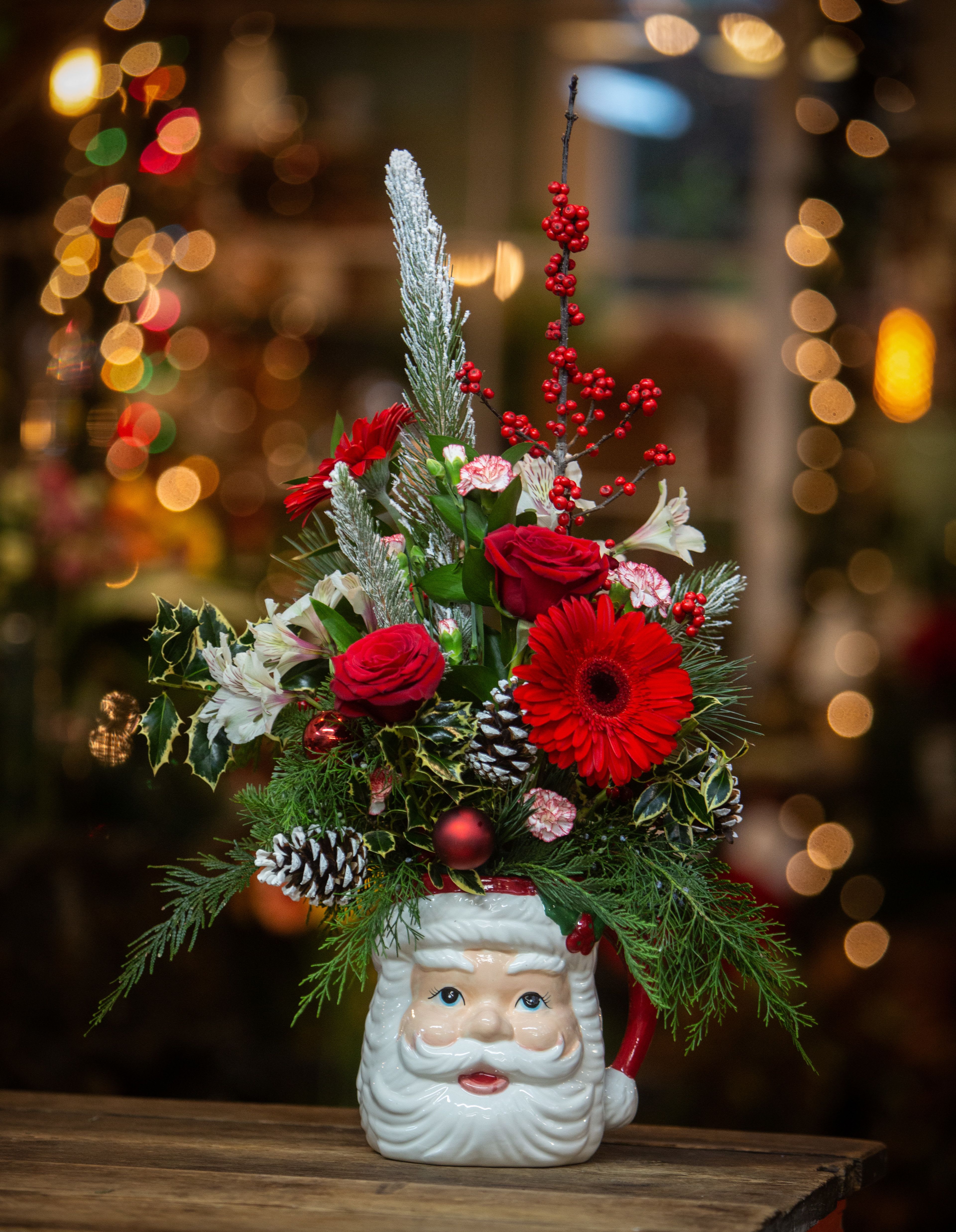 Christmas arrangement in a Santa-face mug with red flowers and pinecones