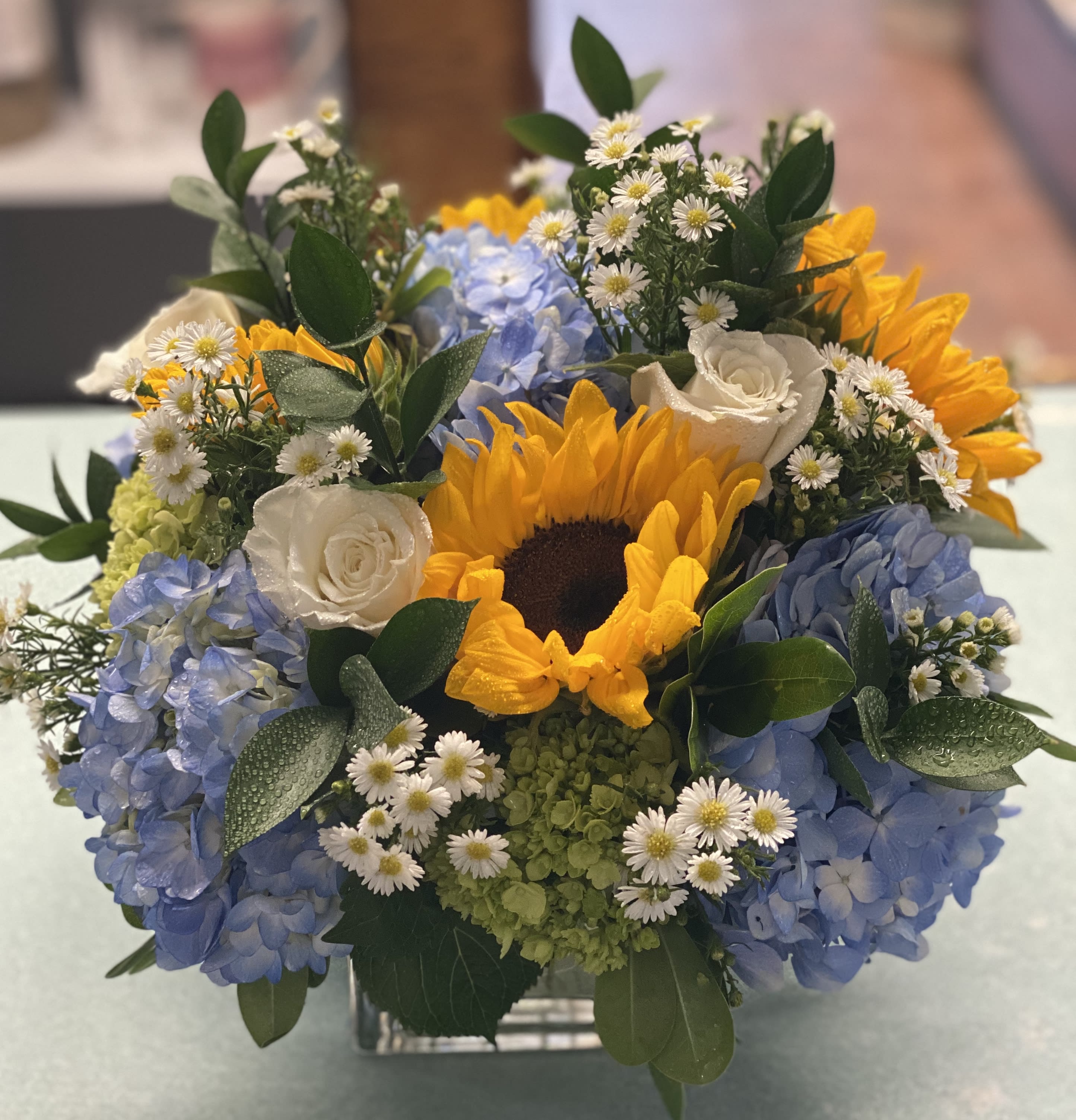Sunflower and blue hydrangea bouquet with white roses in a square vase