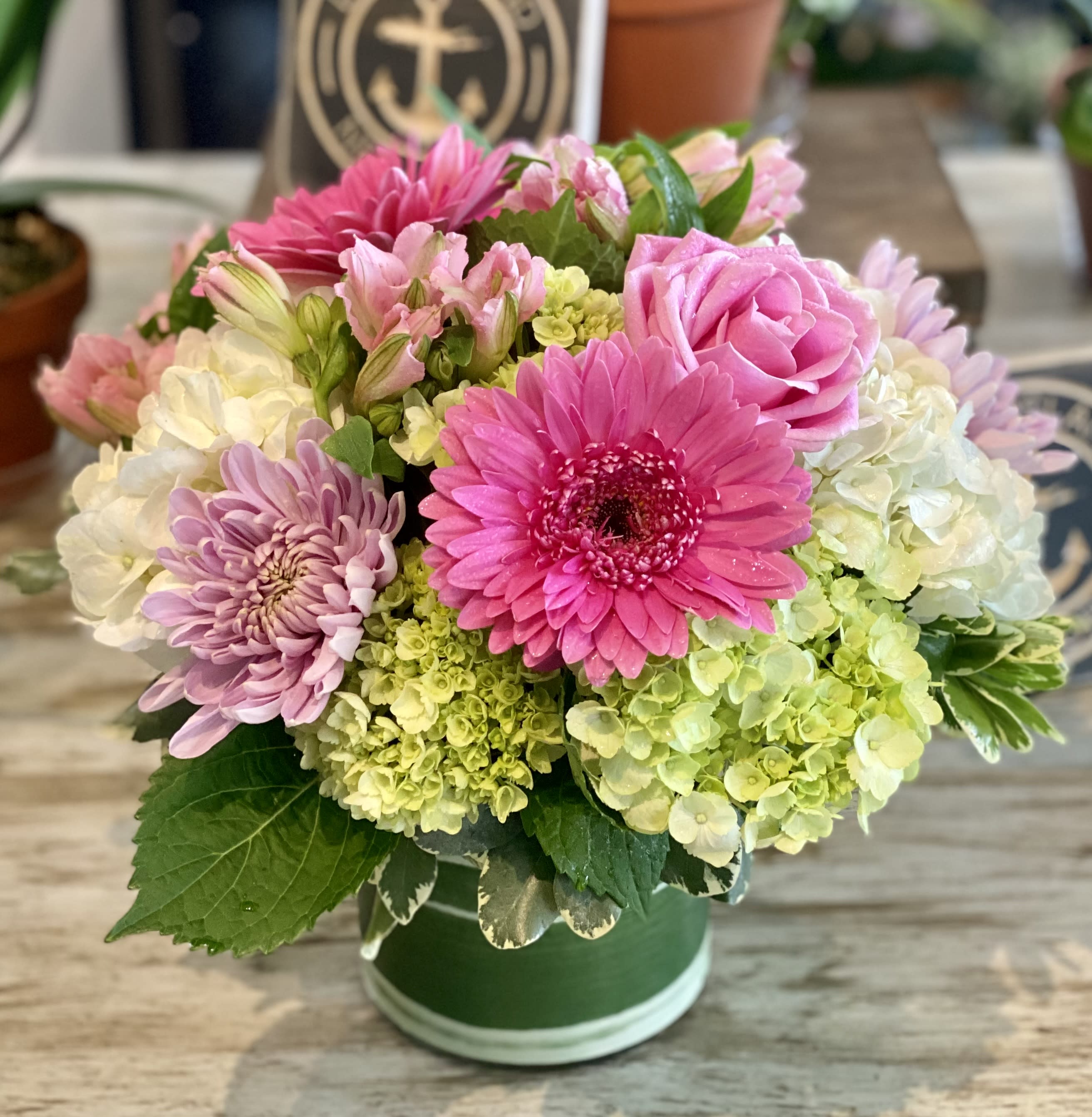 Pink and lavender flowers arranged in a green hatbox