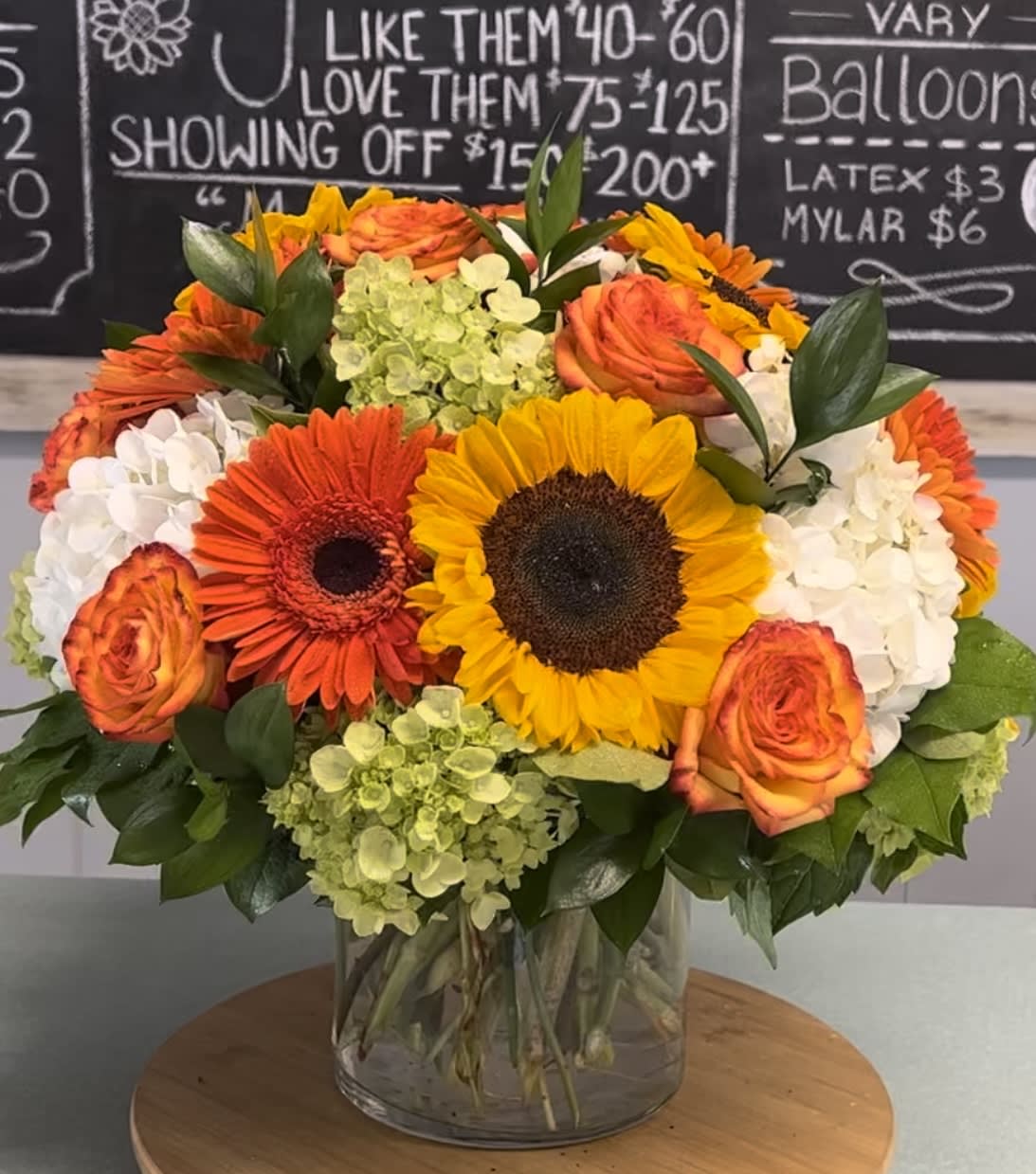 Bouquet of sunflowers, orange roses, and white hydrangeas in a glass vase