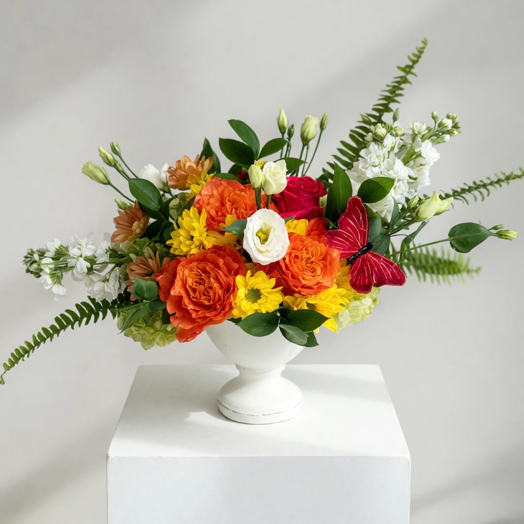 Colorful bouquet in a white pedestal vase with orange, yellow, red, and white blooms