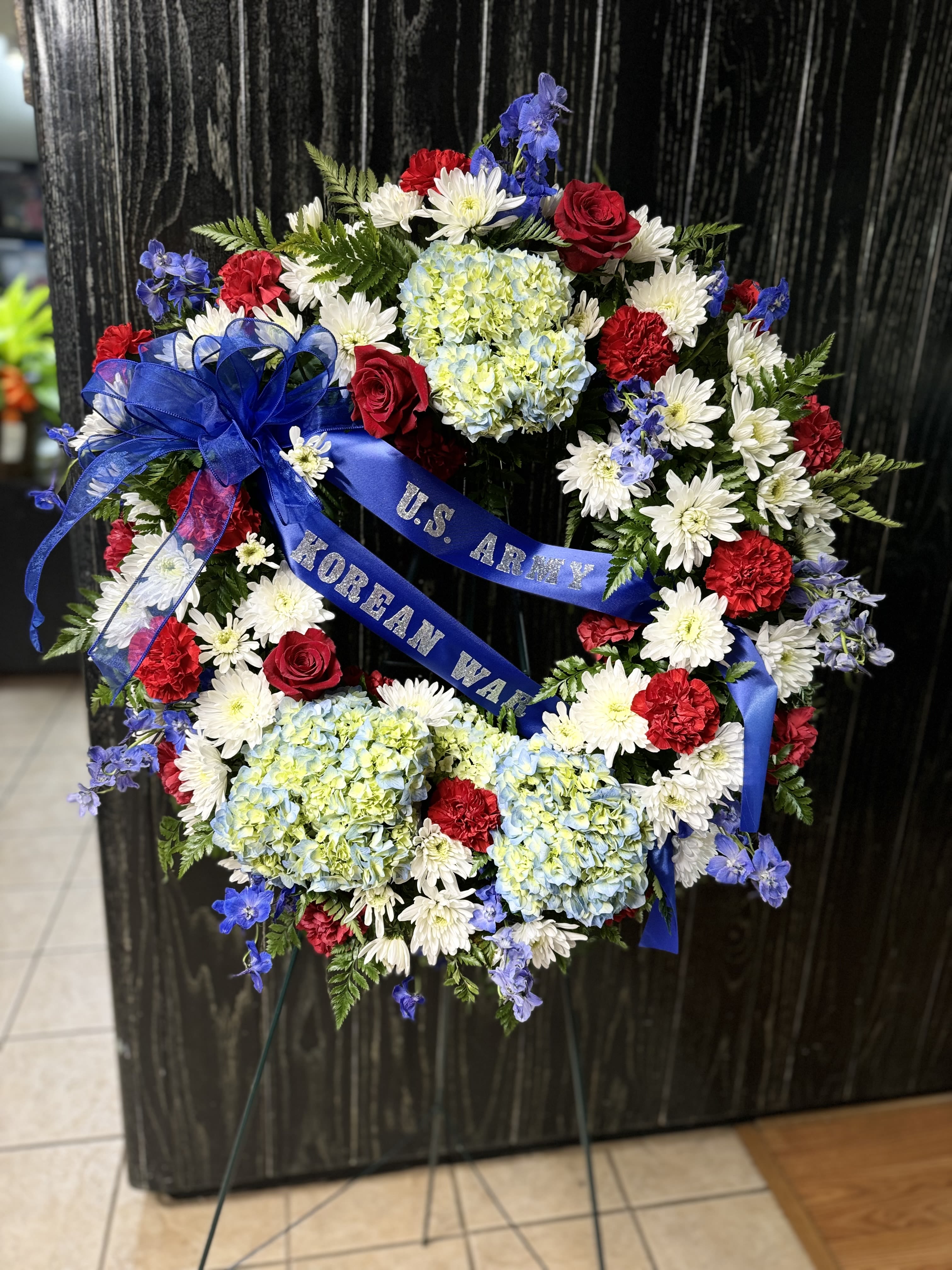 Patriotic funeral wreath with red, white, and blue flowers and a blue ribbon