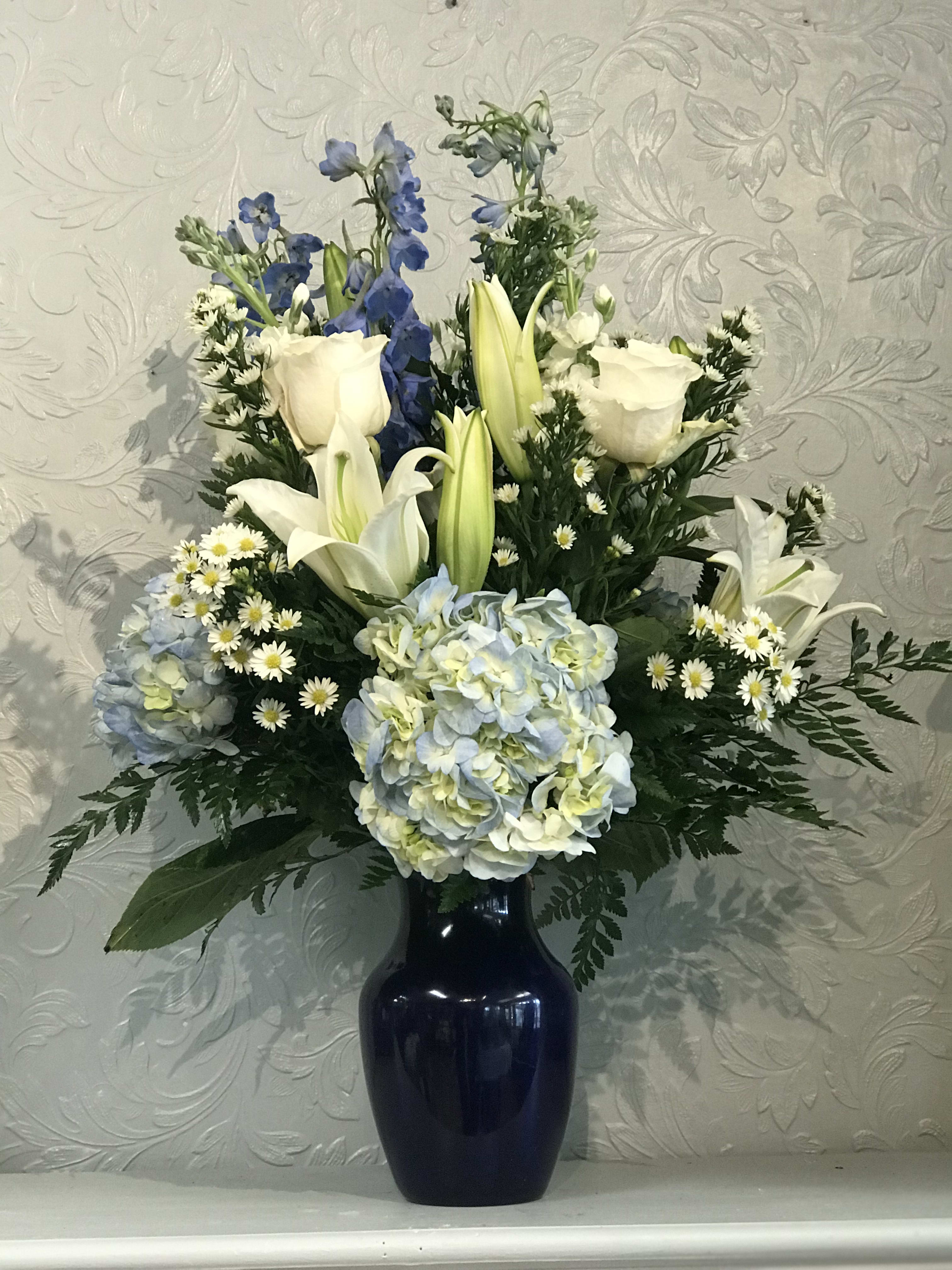 White lilies, roses, and blue flowers in a dark vase