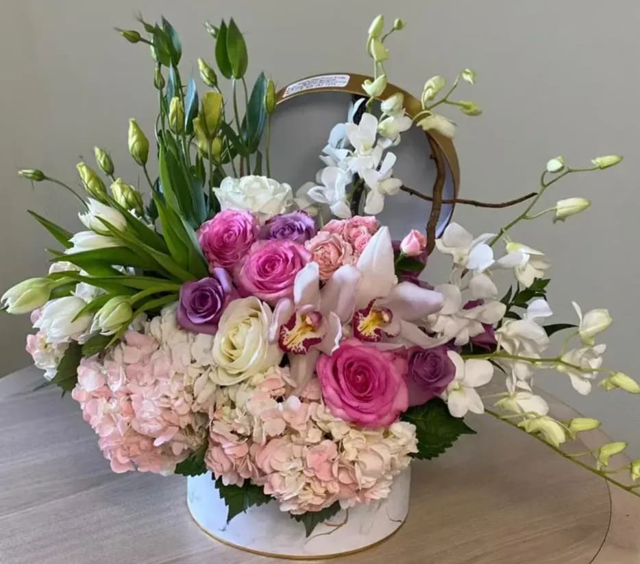 Round box arrangement of pink roses, orchids, tulips, hydrangeas and white orchids with green buds