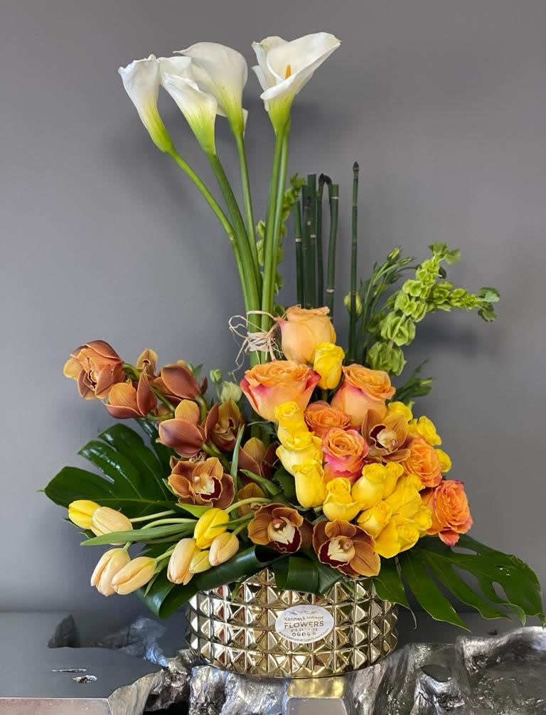 Tall floral arrangement with white calla lilies, roses, and orchids in a gold vase