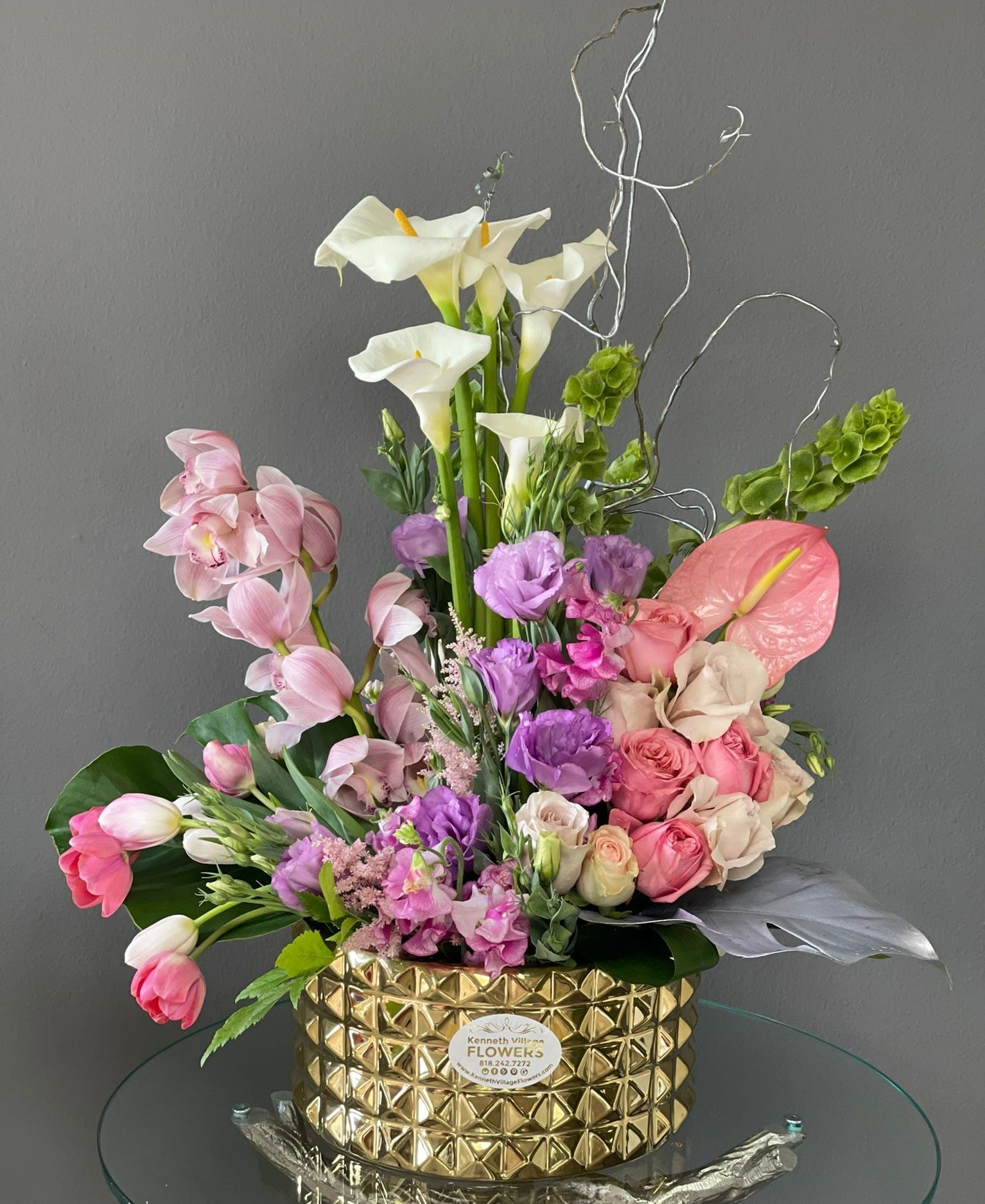 Mixed bouquet with white calla lilies, pink orchids, and roses in a gold vase