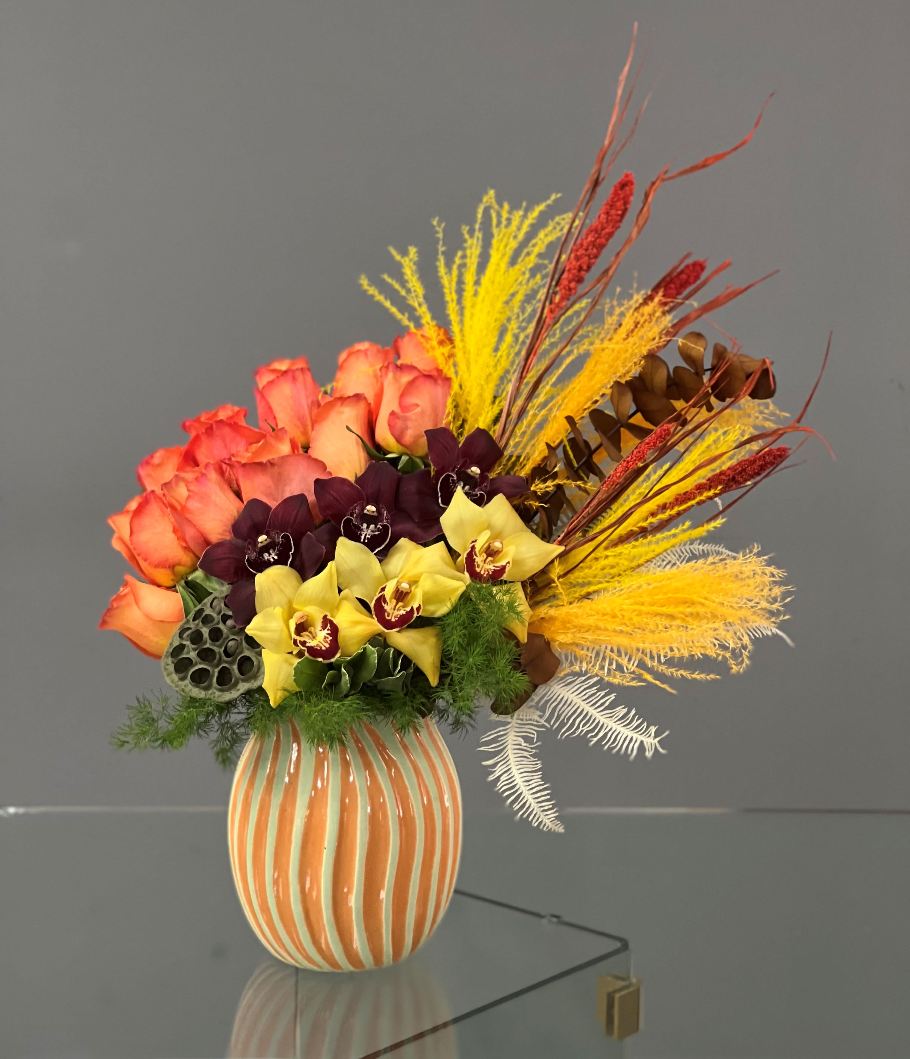 Bouquet of orange roses and yellow orchids in a striped vase