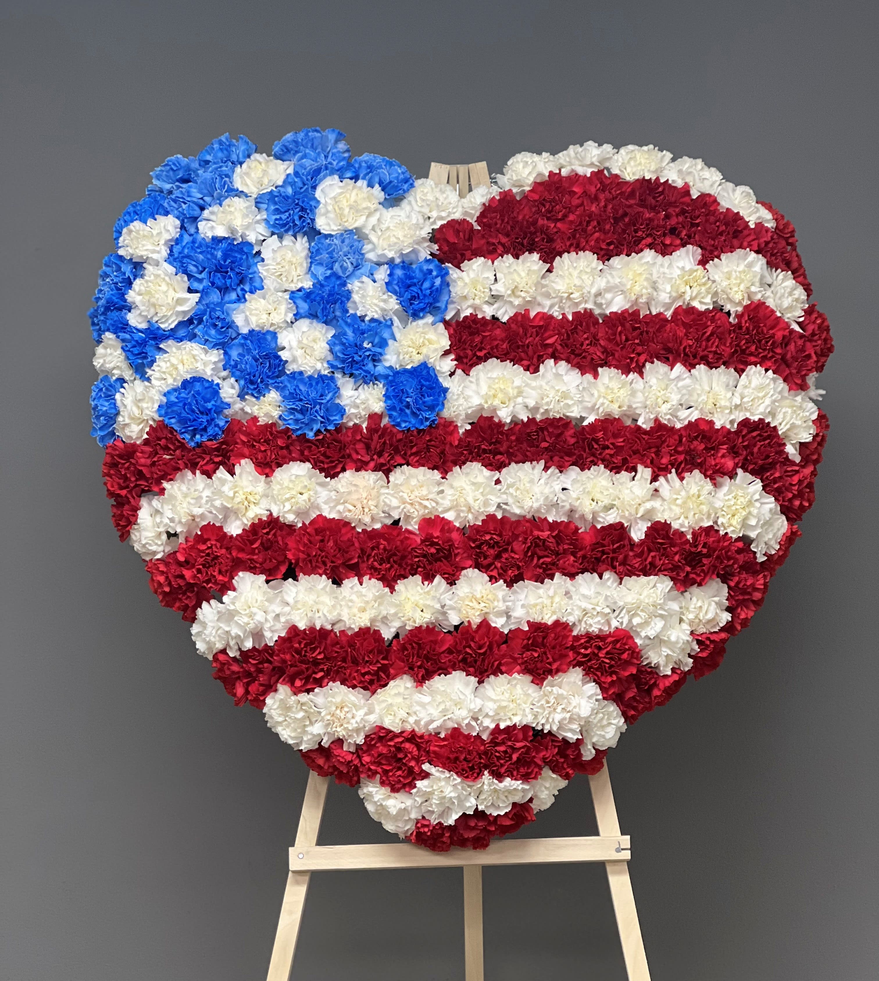 Patriotic Heart Standing Spray - Red, white and blue carnations in the shape of a heart, symbolizing the American flag, create a patriotic display that will celebrate devotion and service to one’s country. A lovely tribute to a veteran or member of the United States armed forces.