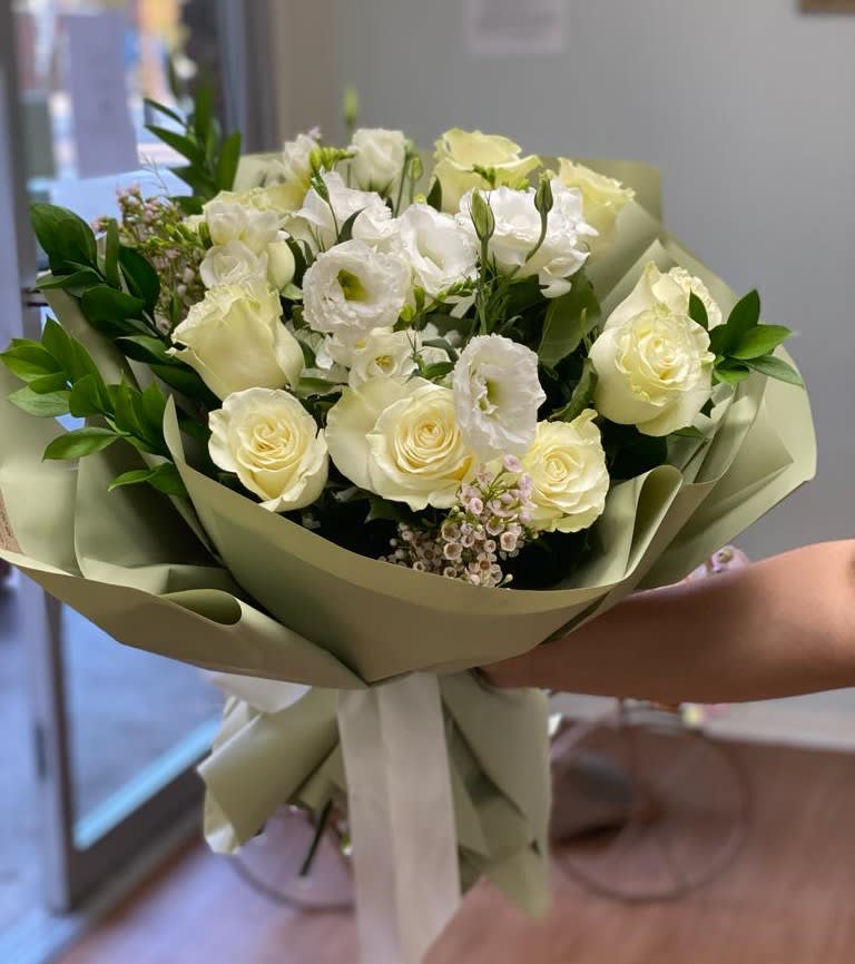 Bouquet of white and pale yellow roses with white blooms wrapped in sage paper