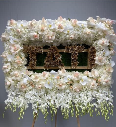 Large white floral standing arrangement on an easel with a central sign