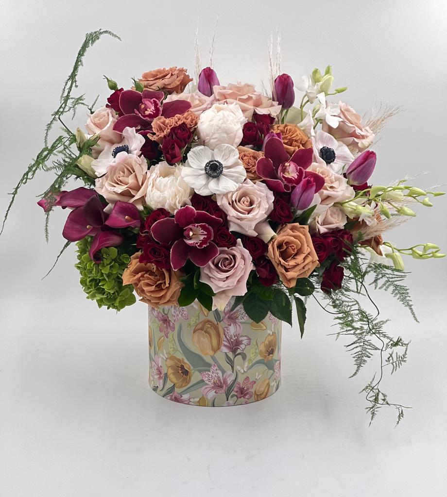 Mixed bouquet of roses, orchids, and tulips in a floral-patterned box