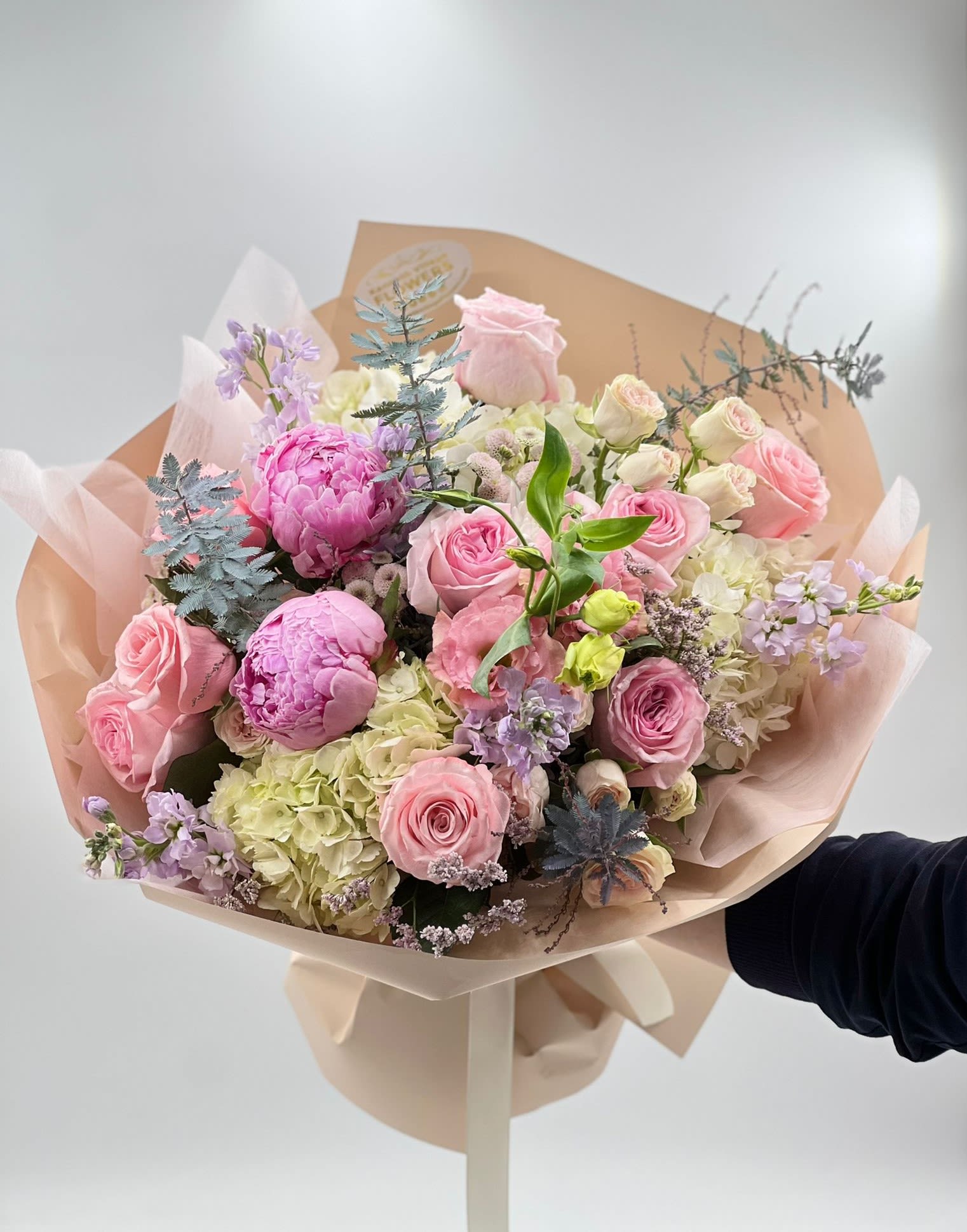 Hand-tied bouquet of pink roses, peonies, and hydrangeas in blush wrap