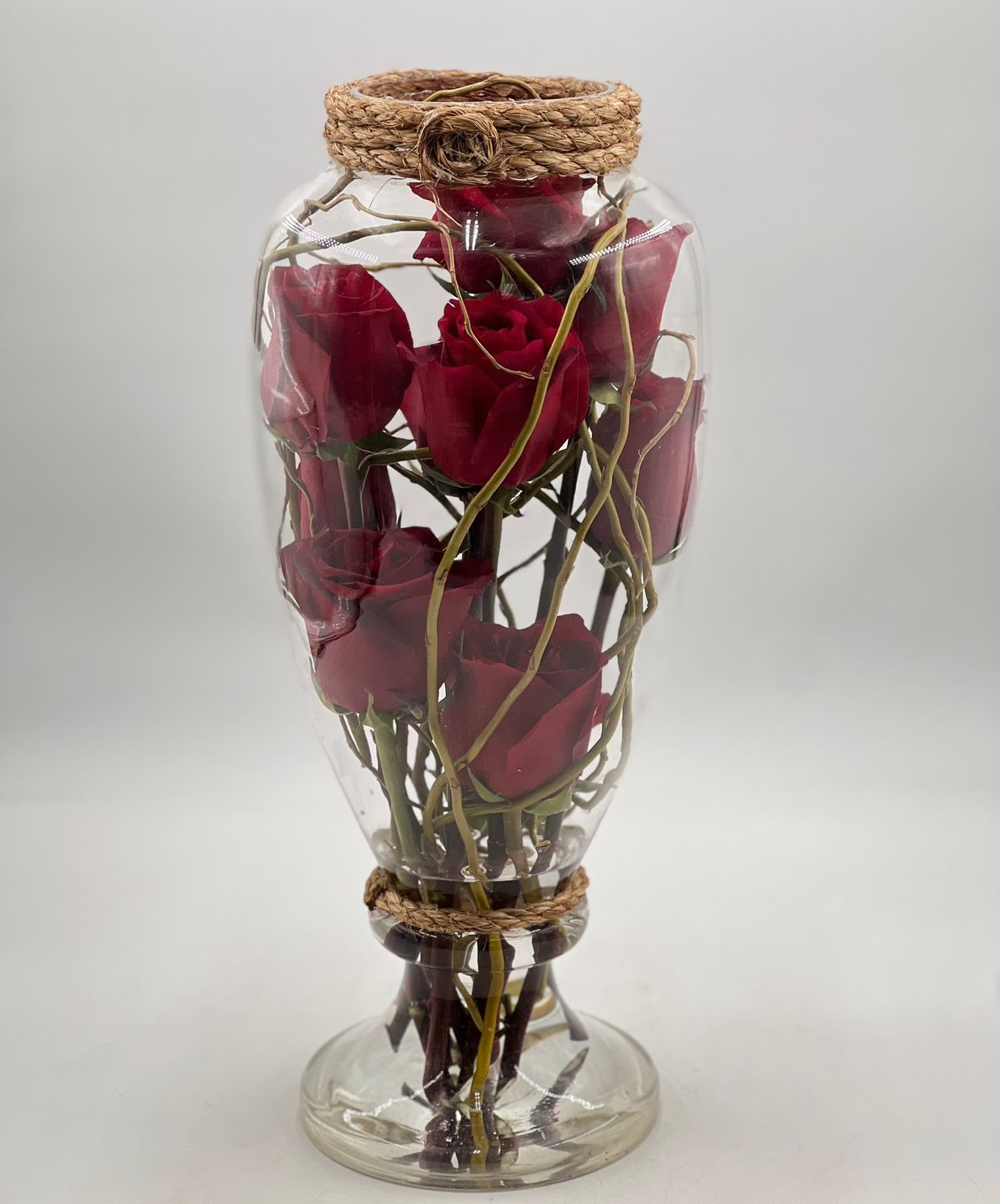Tall clear glass jar filled with red roses and twigs, accented with rope wrapping.