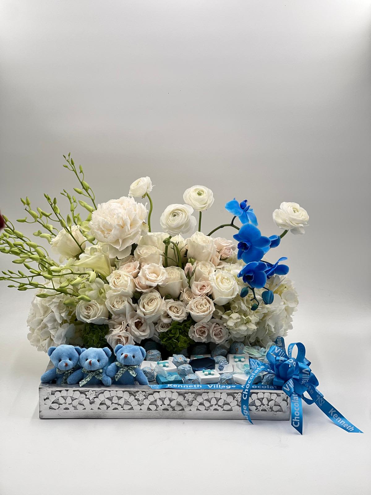 White rose arrangement with blue orchids and small teddy bears in a gift box