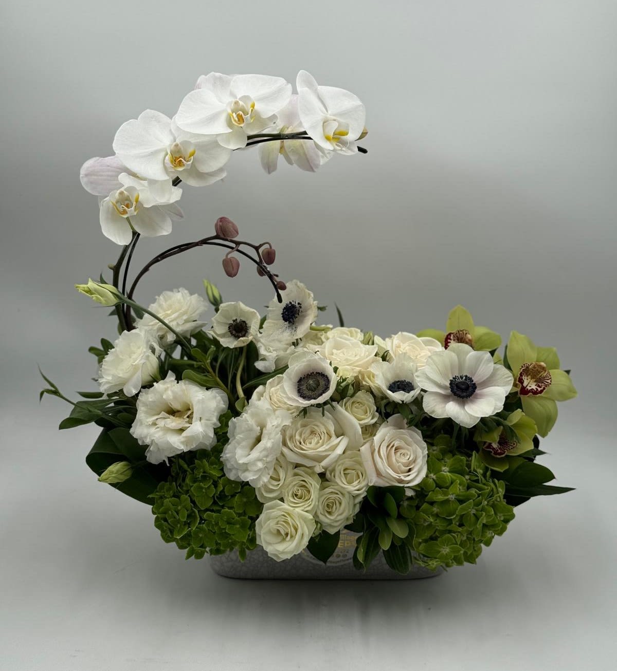 White orchids and roses arranged in a low rectangular container