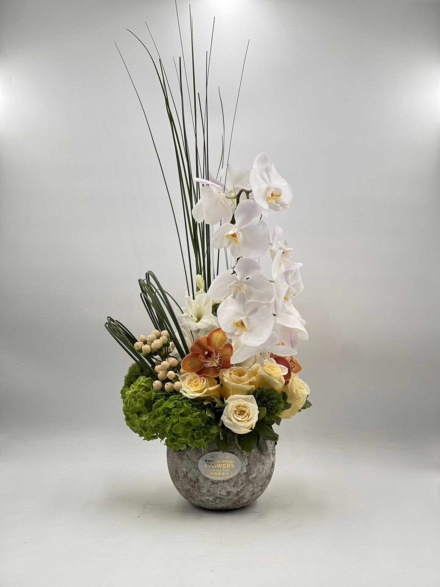 Tall floral arrangement with white orchids and cream roses in a gray vase