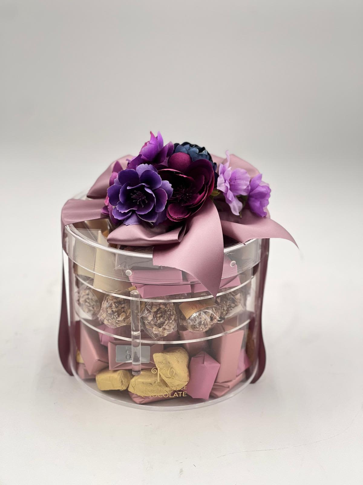 Gift box with purple flowers and chocolates in a clear round container