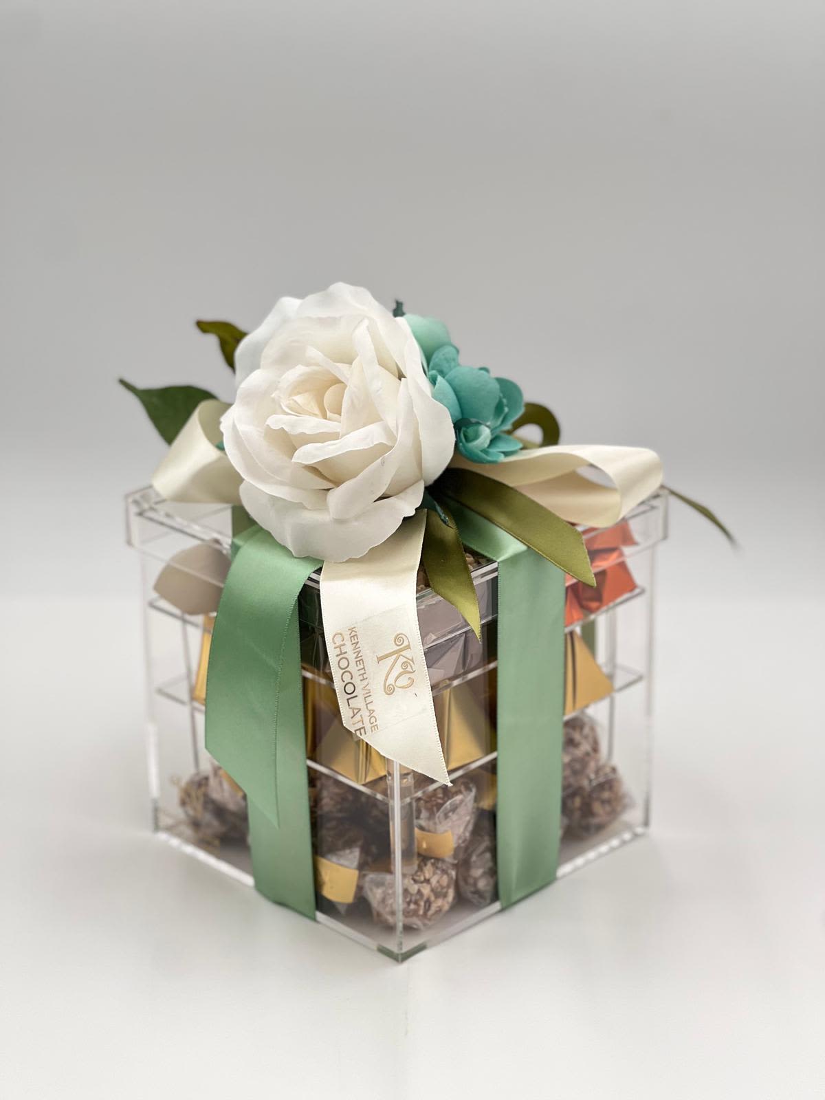 Gift box topped with white and teal flowers and satin ribbons