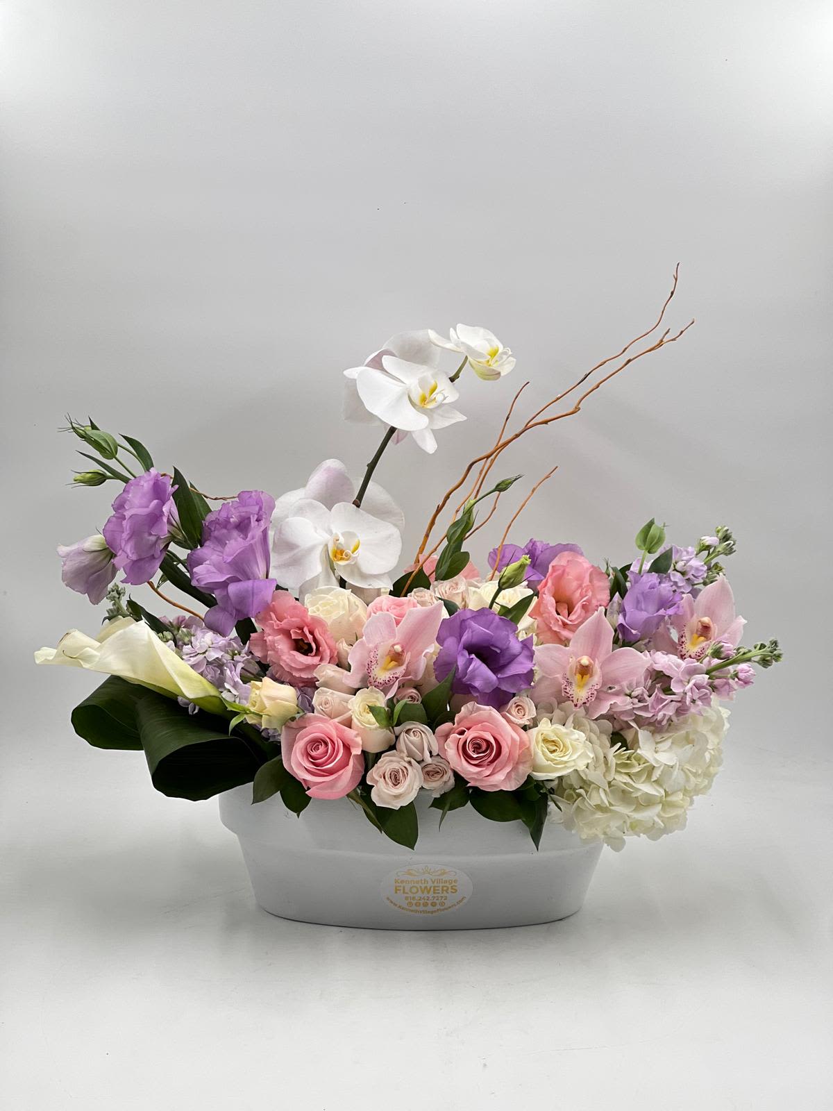 Pastel floral arrangement in a white container with orchids, roses, and hydrangea