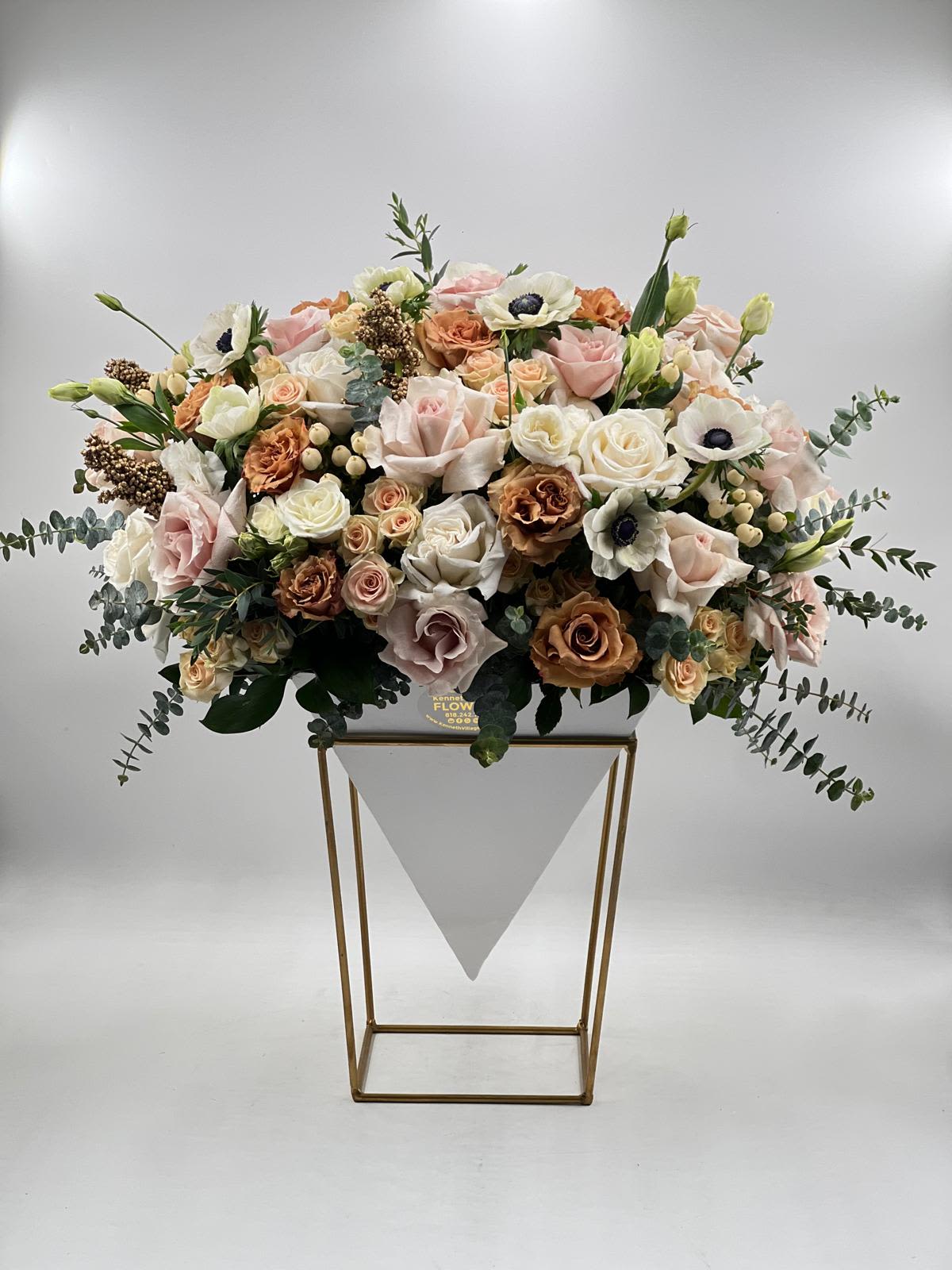Large pastel floral arrangement in a white container on a gold stand