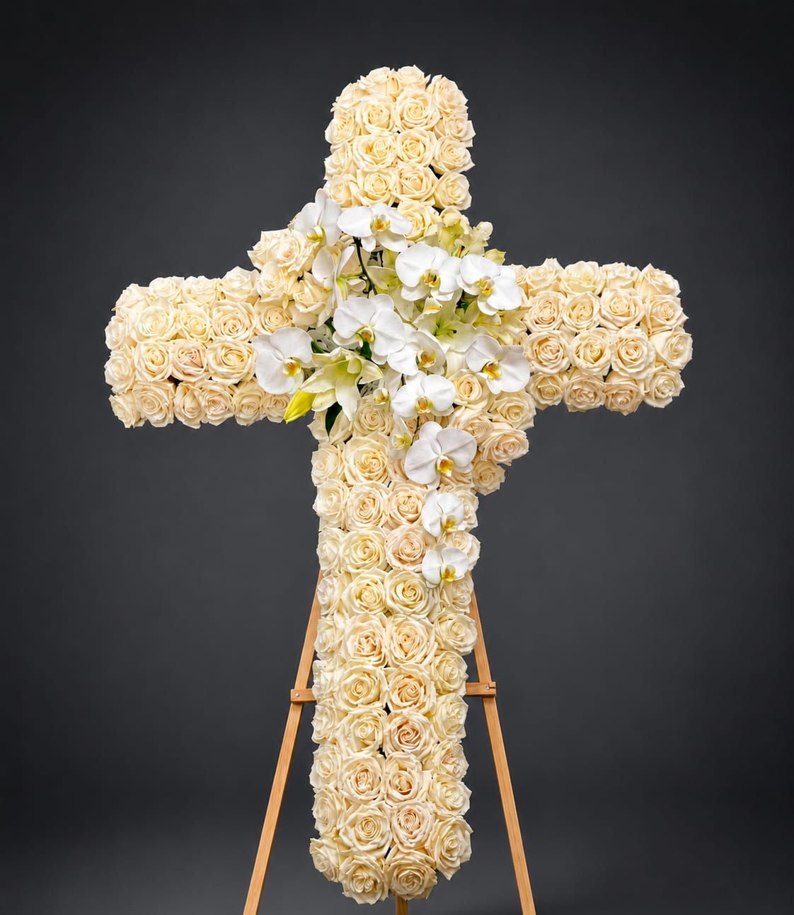 White Rose Cross with Orchids - This elegant sympathy arrangement features a beautifully crafted cross made entirely of white roses, symbolizing peace and eternal love. Accented with cascading white orchids for a touch of grace and purity, the piece stands on a wooden easel and is thoughtfully designed to convey comfort and heartfelt condolences. Perfect for memorial services, church ceremonies and life celebrations.