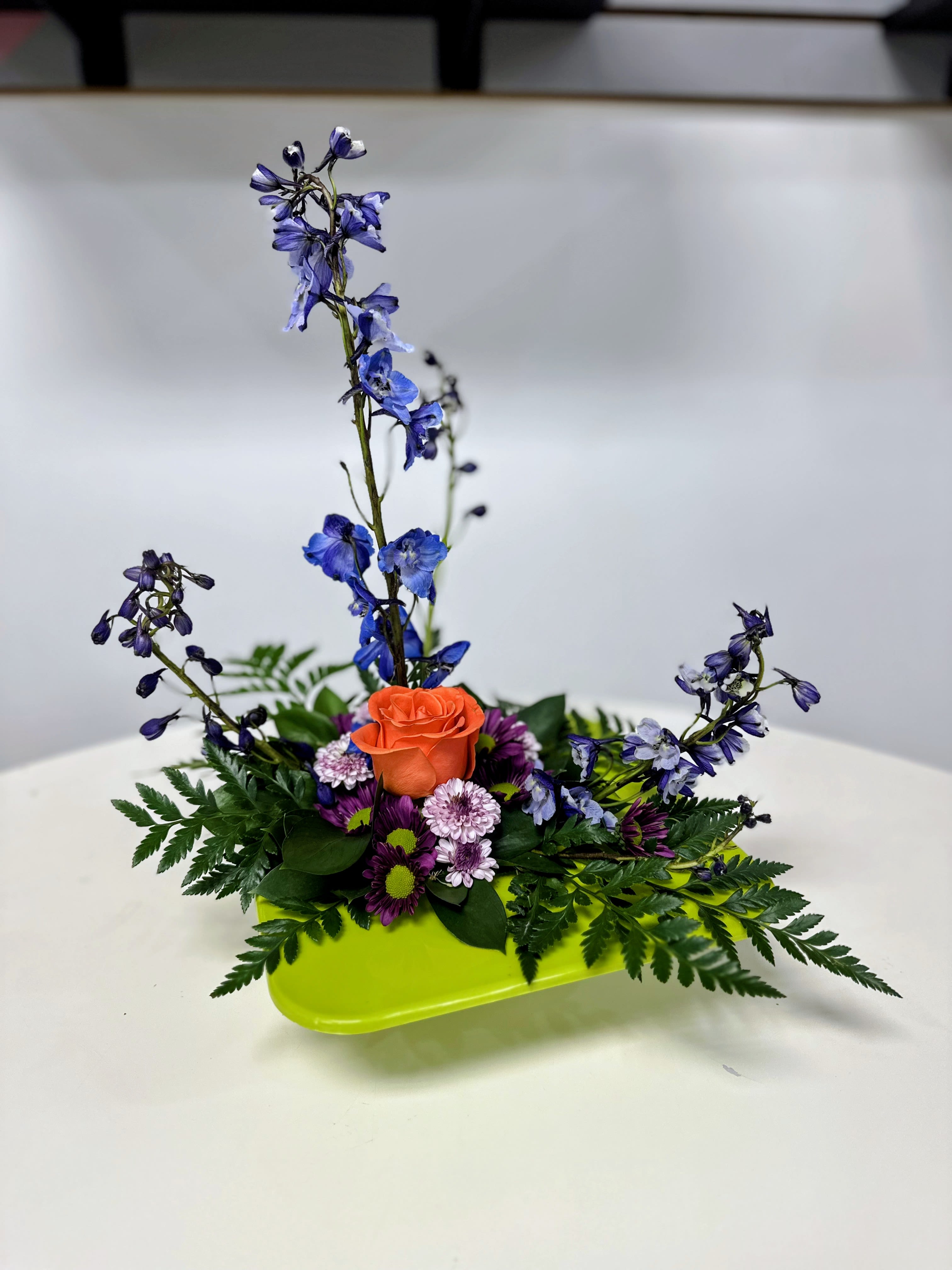 Orange rose and purple flowers in a lime-green tray