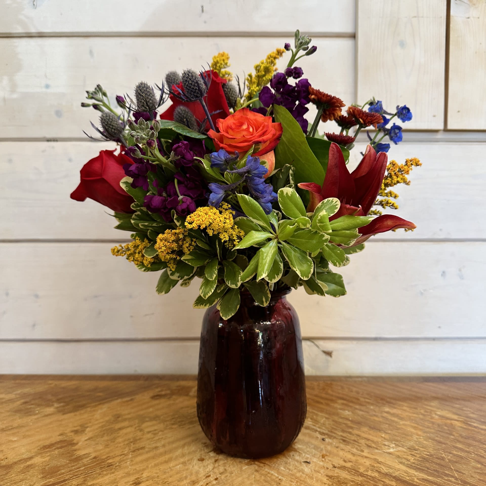 Mixed bouquet of red, orange, purple, and yellow flowers in a dark glass vase