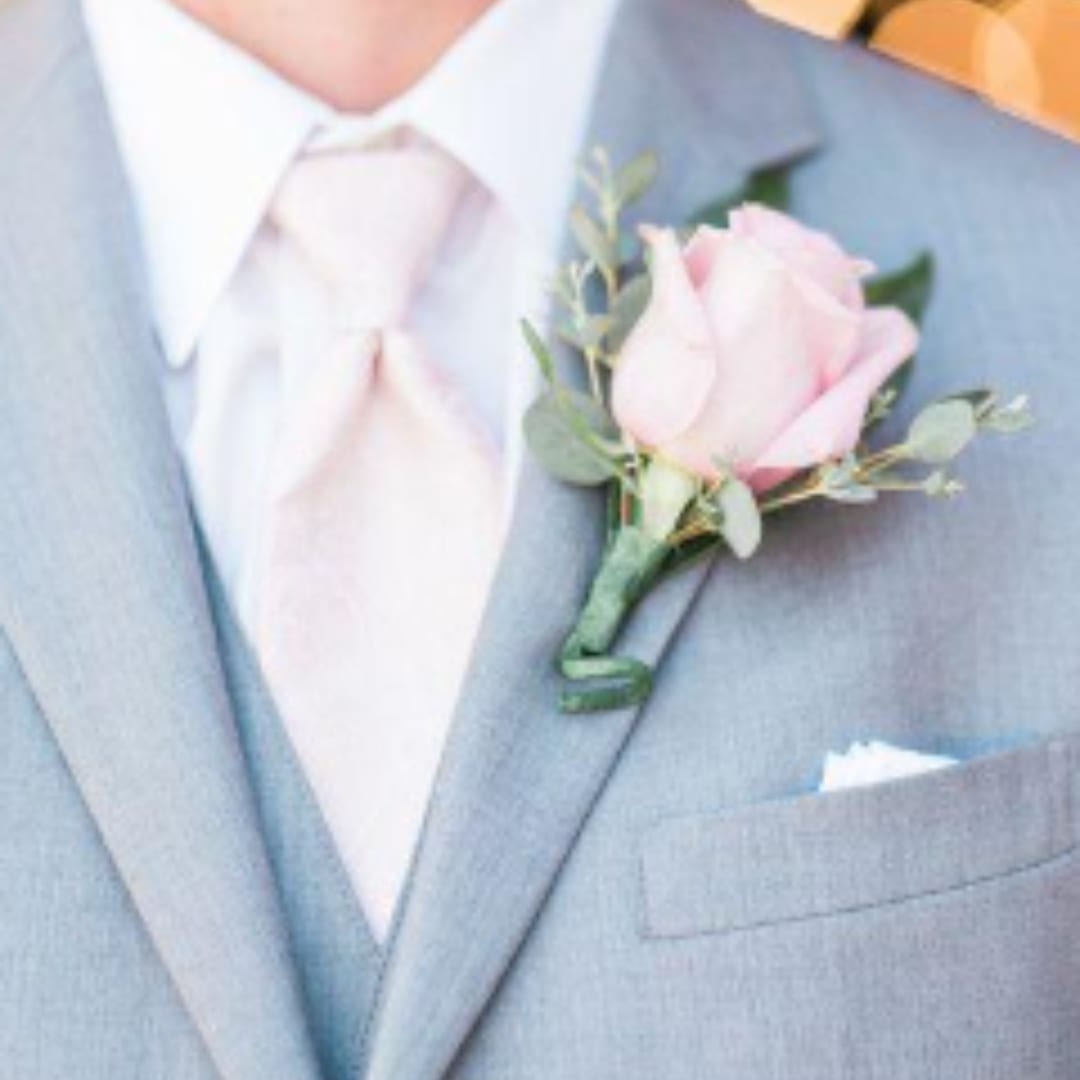 Pink rose boutonniere pinned to a light blue suit jacket