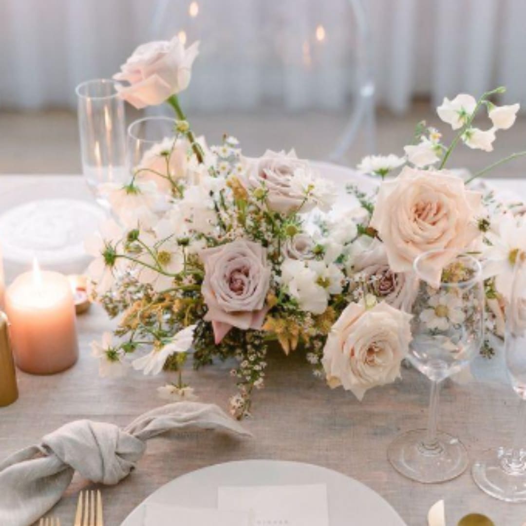 Low wedding centerpiece with pale roses and white flowers on a table