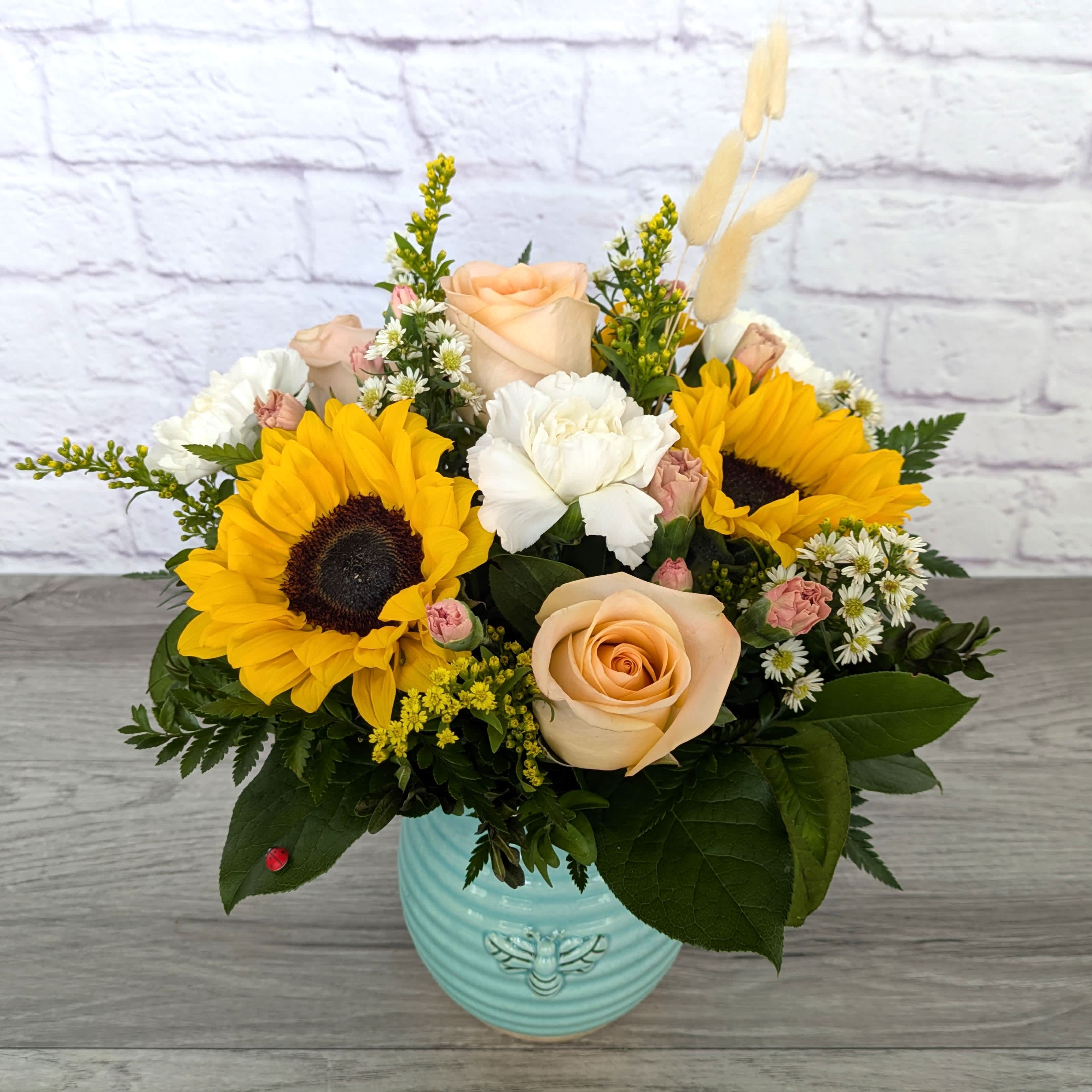 Mixed bouquet with sunflowers, roses, and white blooms in a blue vase